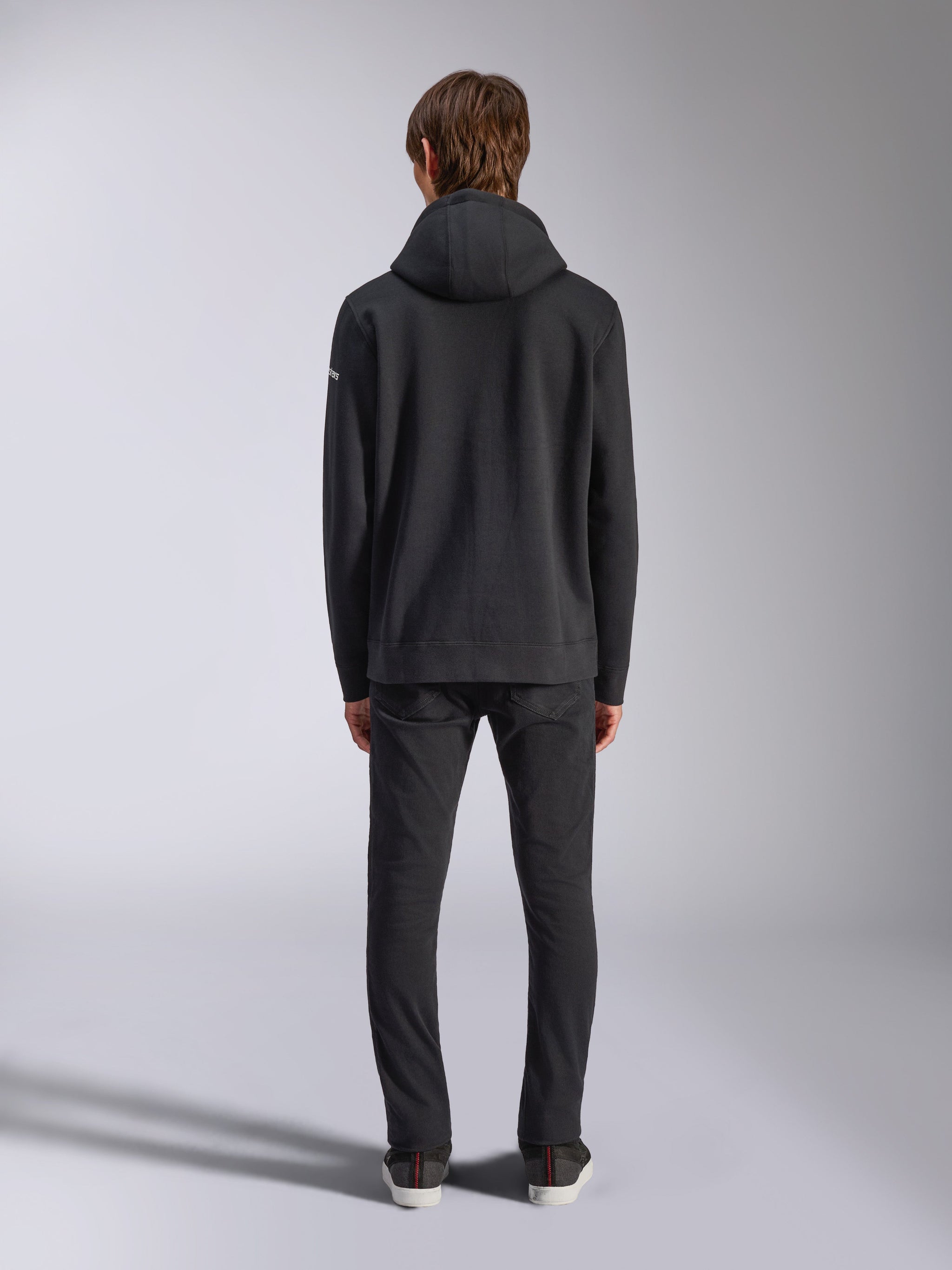 Alpinestars Frontal Hoodie, casual streetwear, black, rear view of model wearing pullover fleece hoodie, featuring ribbed hem and cuffs, small white wordmark logo on sleeve, paired with black pants