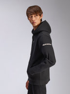 Alpinestars Frontal Hoodie, hoodie de lã preto, modelo visto de perfil lateral, logótipo Alpinestars branco na manga, bolso canguru, streetwear casual inspirado no desporto motorizado