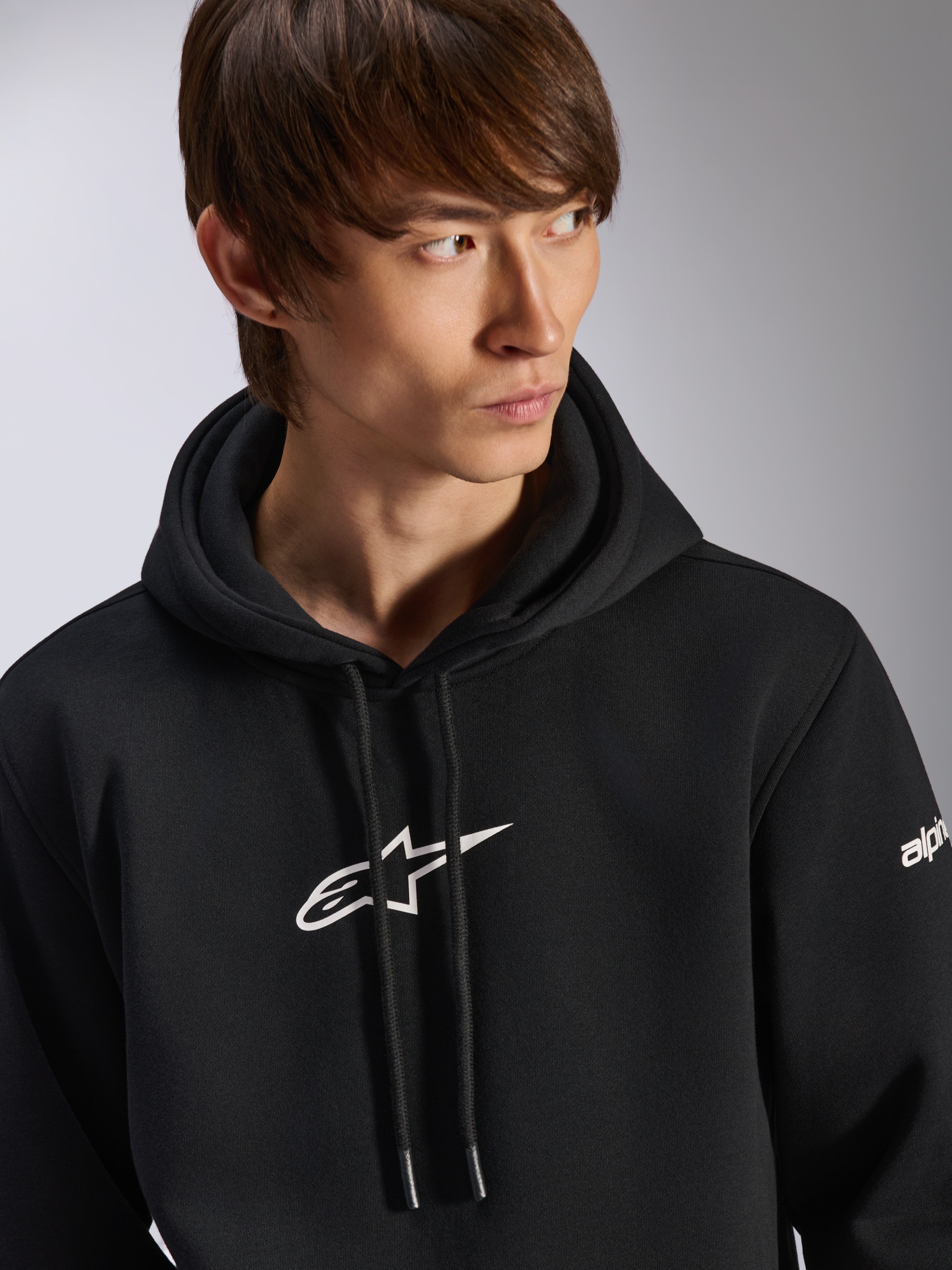 Alpinestars Frontal Hoodie, hoodie de lã preto, logótipo Astar branco no peito e logótipo na manga, capuz com cordão, usado por modelo masculino, streetwear casual de desporto motorizado