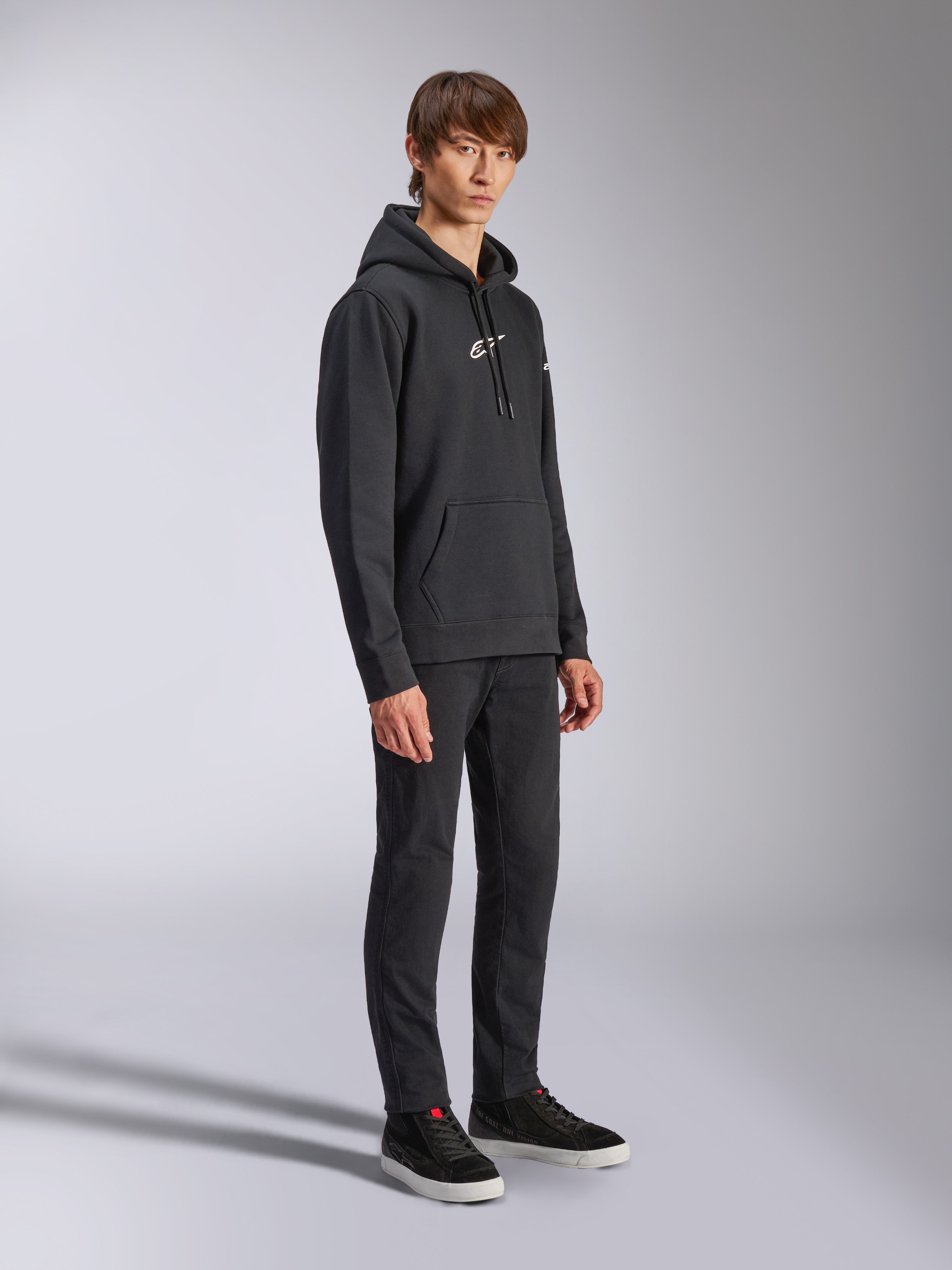 Alpinestars Frontal Hoodie, preto, hoodie de lã com capuz com logótipo HD branco no peito e logótipos de marca nas mangas, bolso canguru, combinado com calças e sapatilhas pretas, streetwear casual inspirado no desporto motorizado