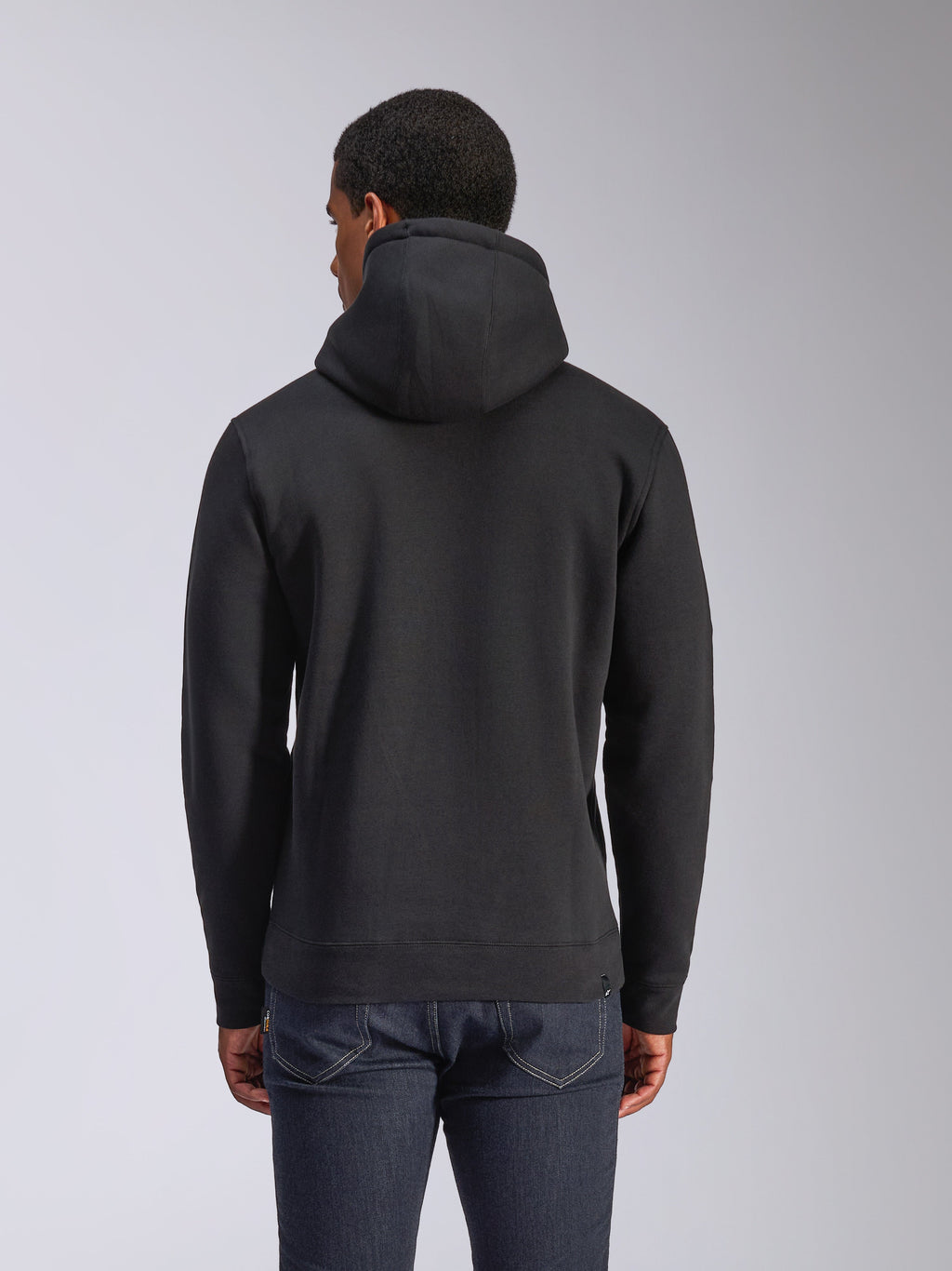 Alpinestars Blaze V3 Hoodie, vista traseira de hoodie preto em fleece, streetwear casual, com punhos e bainha canelados, capuz forrado em jersey, usado com calças de ganga azul escuro