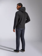 Alpinestars Blaze V3 Hoodie, vista traseira de um homem a usar a camisola preta com capuz, combinada com calças de ganga escuras e sapatilhas pretas, streetwear casual inspirado no desporto motorizado