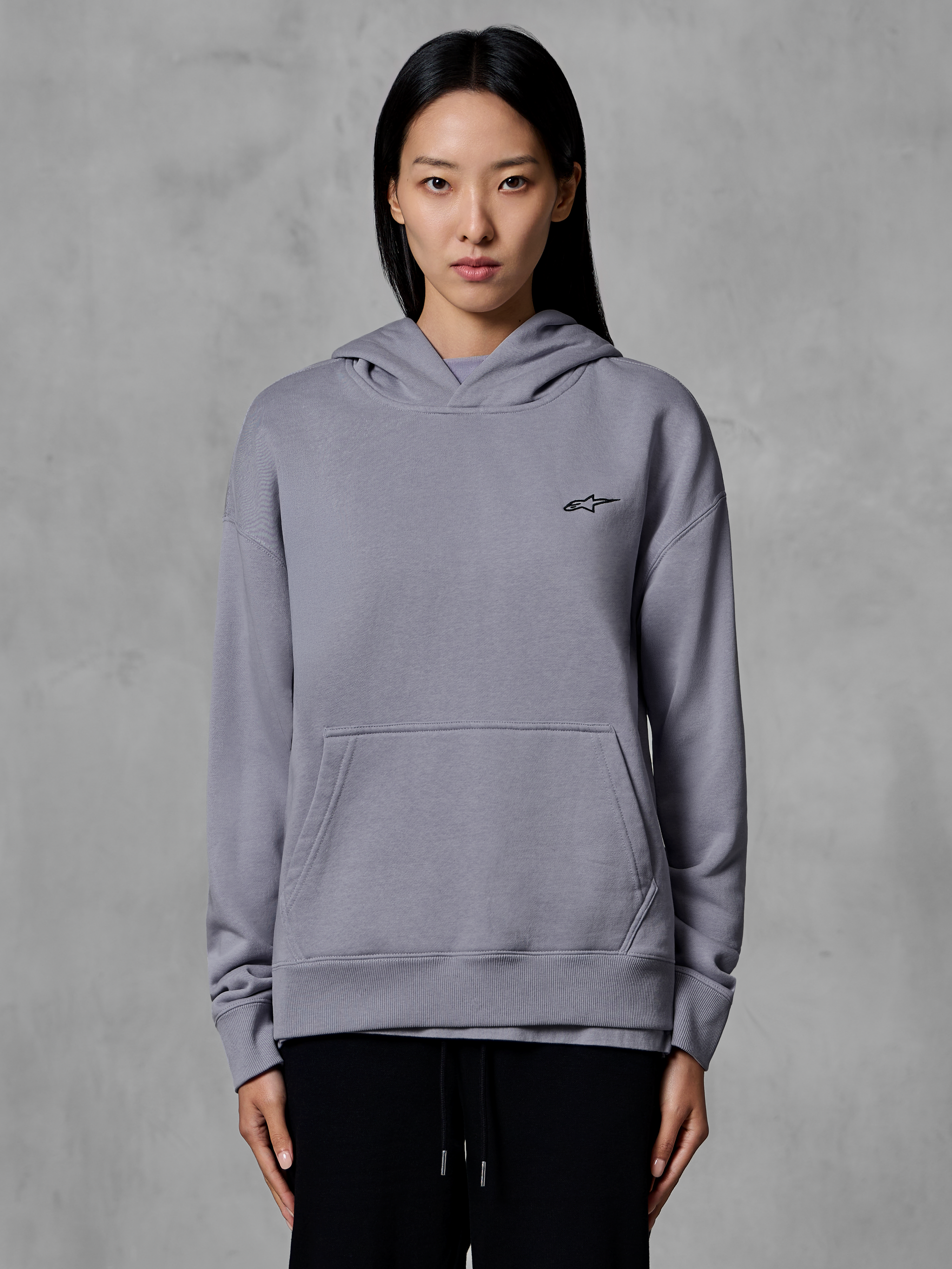 Hoodie Alpinestars Essentials Ageless, roupa desportiva casual, prateado com pequeno logótipo preto, bolso tipo canguru, pulôver com capuz, usado por modelo, vestuário de estilo de vida moderno