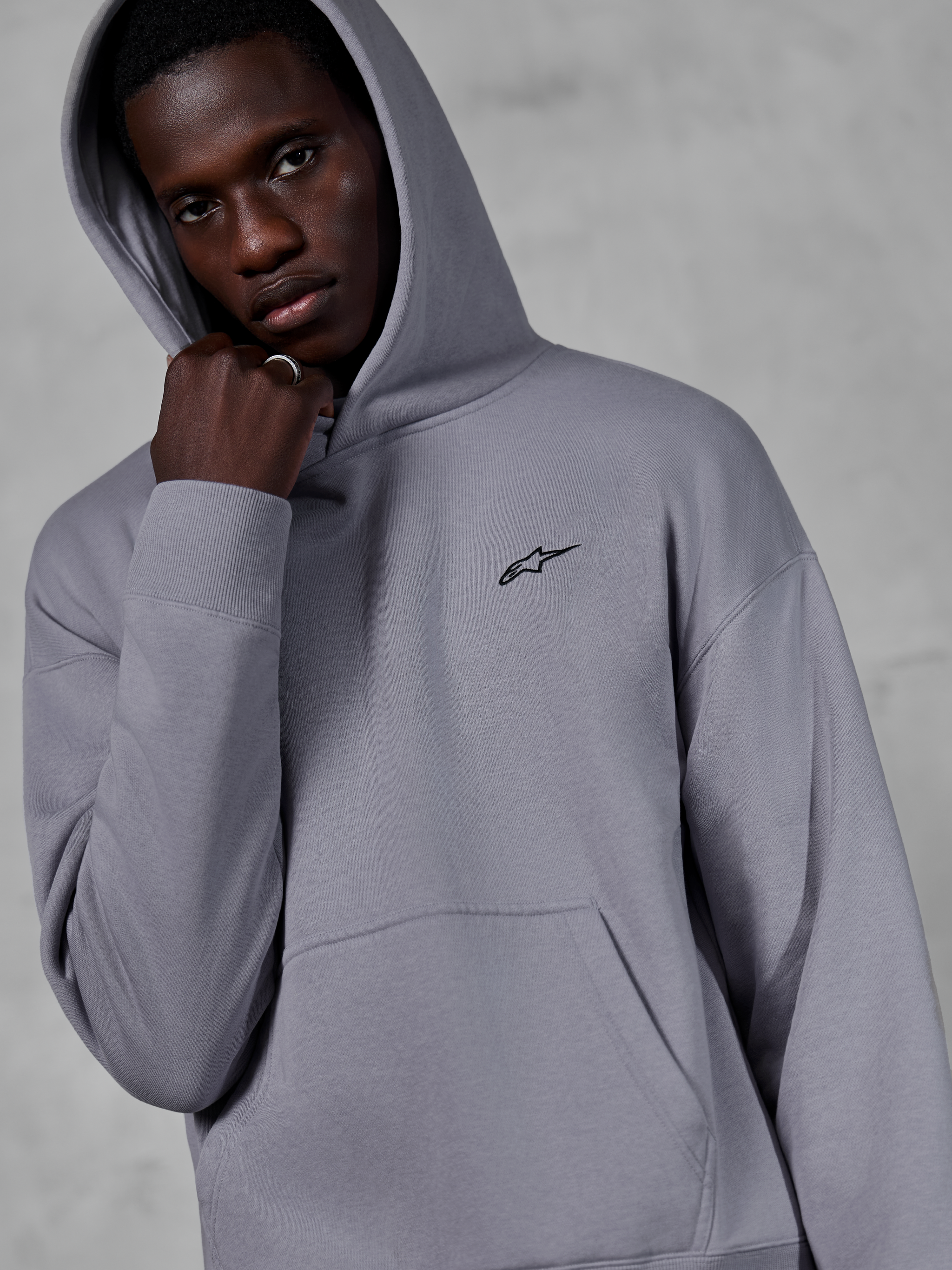 Alpinestars Essentials Ageless Hoodie, Silver, modelo masculino a usar o hoodie com o capuz levantado, pequeno logótipo Alpinestars preto no peito, bolso canguru, punhos canelados, estilo casual streetwear
