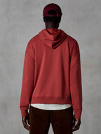 Alpinestars Essentials Ageless Hoodie, hoodie casual em fleece, vermelho tijolo, vista traseira de modelo a usar vestuário lifestyle, com um design simples, bainha e punhos canelados, combinado com calças de bombazina castanhas e boné bordeaux