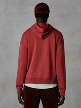 Alpinestars Essentials Ageless Hoodie, hoodie casual em fleece, vermelho tijolo, vista traseira de modelo a usar vestuário lifestyle, com um design simples, bainha e punhos canelados, combinado com calças de bombazina castanhas e boné bordeaux