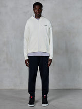 Alpinestars Essentials Ageless Zip Hoodie, hoodie de fecho completo Off White, ajuste relaxado com pequeno logótipo preto no peito, usado com calças de fato de treino pretas e sapatilhas, streetwear casual inspirado no desporto motorizado.