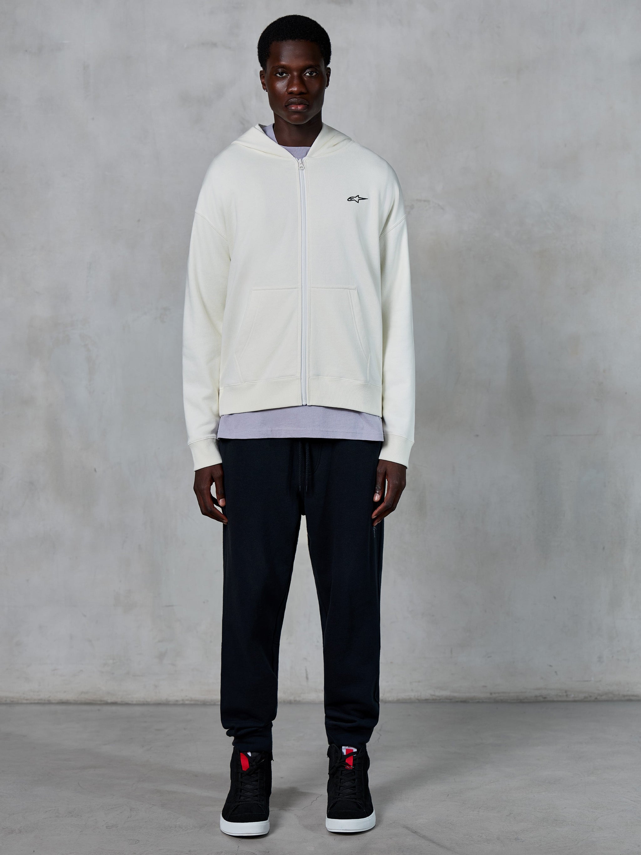 Alpinestars Essentials Ageless Zip Hoodie, hoodie de fecho completo Off White, ajuste relaxado com pequeno logótipo preto no peito, usado com calças de fato de treino pretas e sapatilhas, streetwear casual inspirado no desporto motorizado.