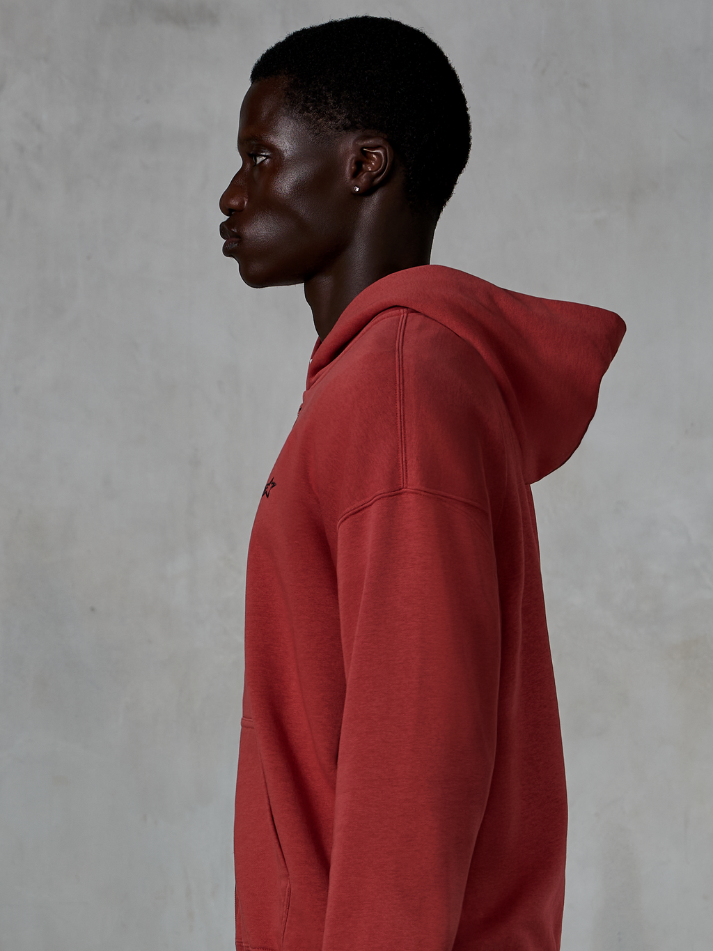 Hoodie Alpinestars Essentials Ageless com fecho, vermelho tijolo, vista de perfil de um homem a usar um hoodie de corte relaxado com fecho, pequeno logótipo de estrela preto no peito, fleece premium com lavagem de pedra, streetwear casual inspirado no desporto motorizado