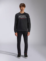 Alpinestars Bettern Crew, camisola de gola redonda preta, apresenta o logótipo Alpinestars em branco com riscas horizontais cinzentas e o texto 'RACING AHEAD' em vermelho, streetwear casual de desportos motorizados, vestida por um modelo com calças pretas e sapatilhas