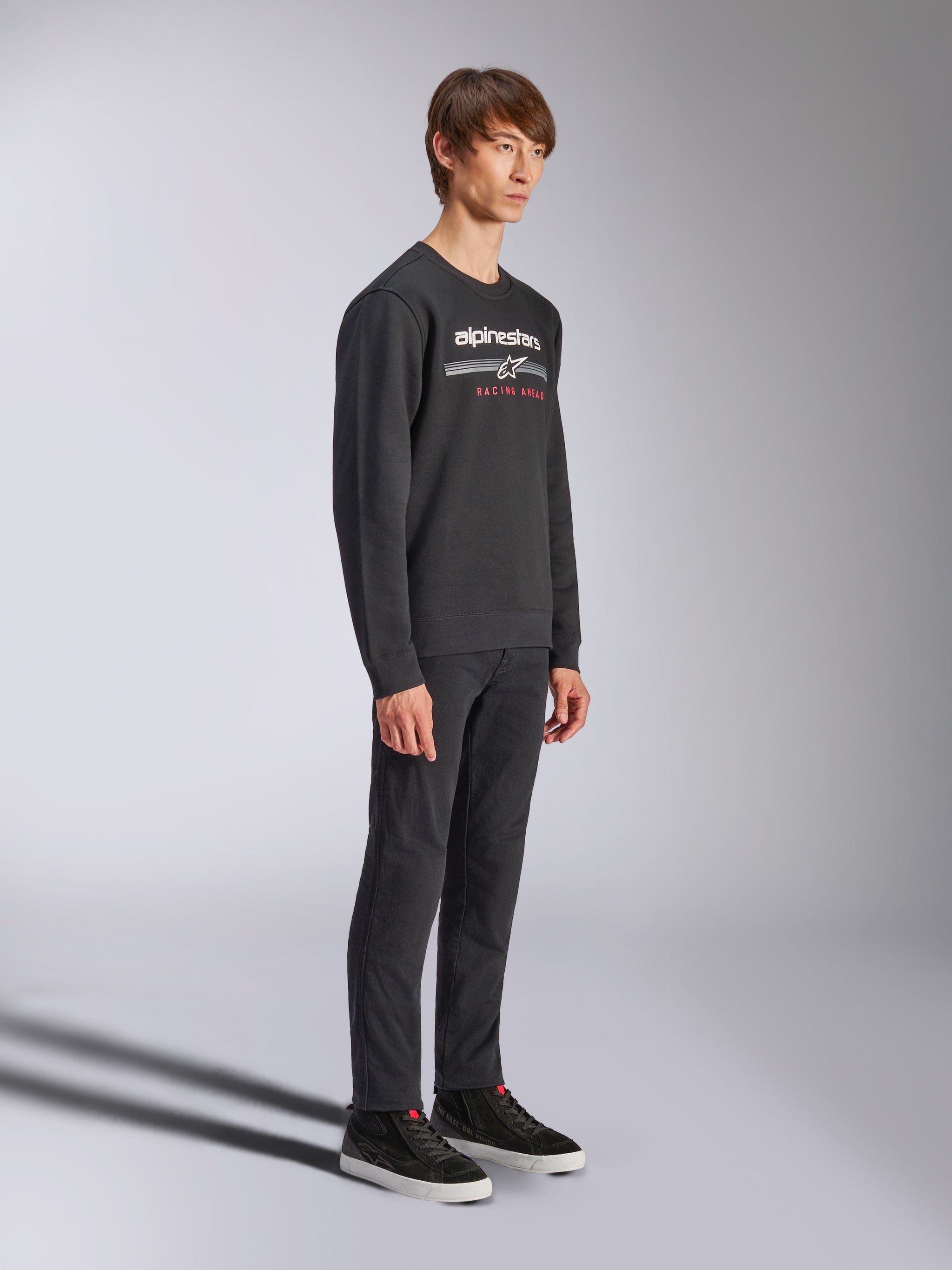 Sweatshirt Alpinestars Bettern Crew, pullover preto de gola redonda, logótipo Alpinestars branco com 'RACING AHEAD' a vermelho no peito, combinado com calças pretas e ténis, streetwear casual inspirado no desporto motorizado