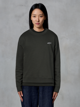 Alpinestars Essentials Ageless Crew, sweatshirt premium de gola redonda, cor Off Black, com um pequeno logótipo branco da Alpinestars no peito, estilo streetwear casual usada por uma modelo com calças de ganga escuras