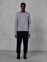 Alpinestars Essentials Ageless Crew, sweatshirt prateada de gola redonda, vestida por um modelo com calças jogger pretas e ténis pretos, com um pequeno logótipo Alpinestars preto no peito, streetwear casual inspirado no desporto motorizado