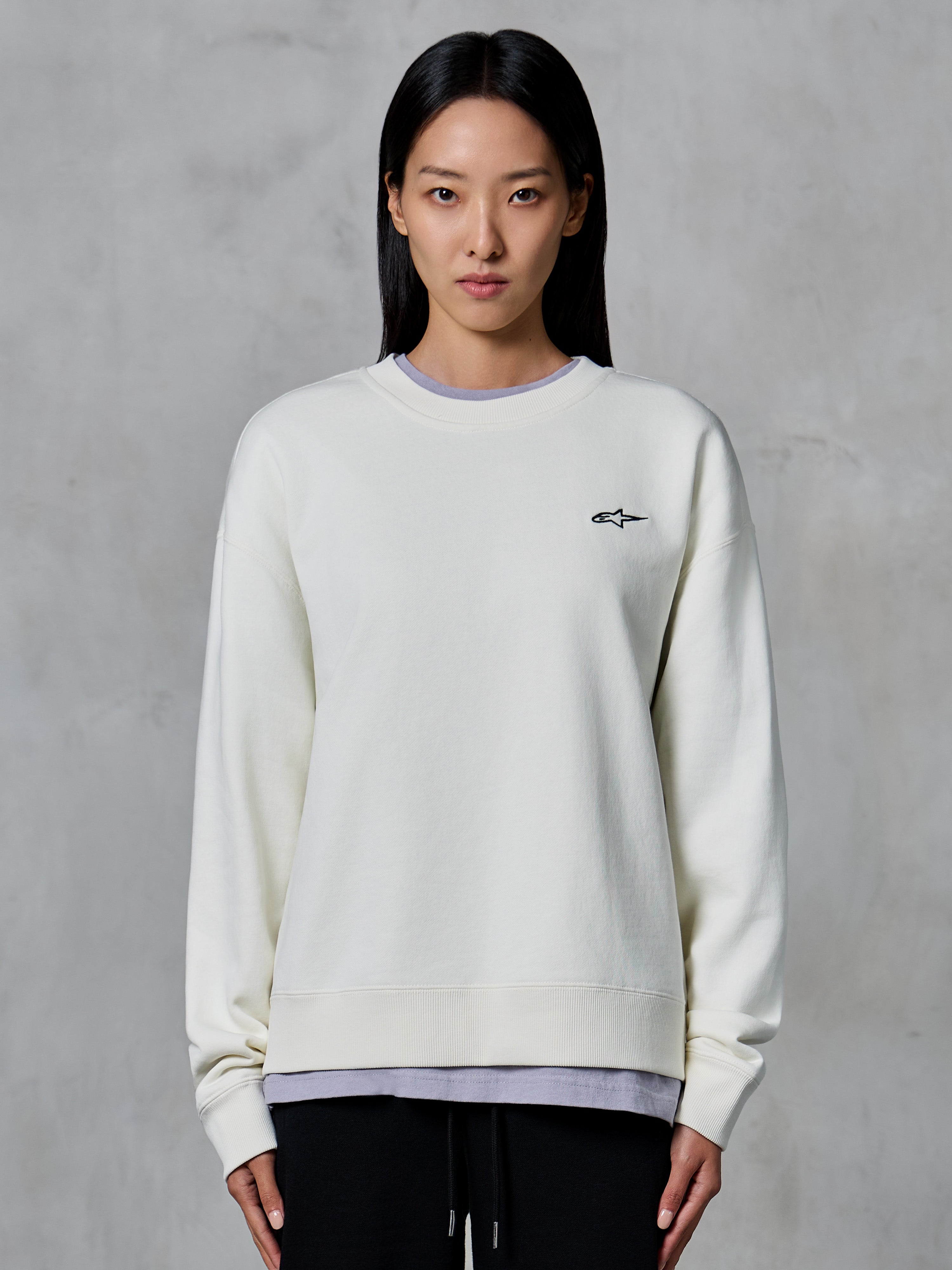 Alpinestars Essentials Ageless Crew, sweatshirt de gola redonda, off white, com um pequeno logótipo preto da Alpinestars no peito, vestuário de estilo de vida casual modelado numa mulher