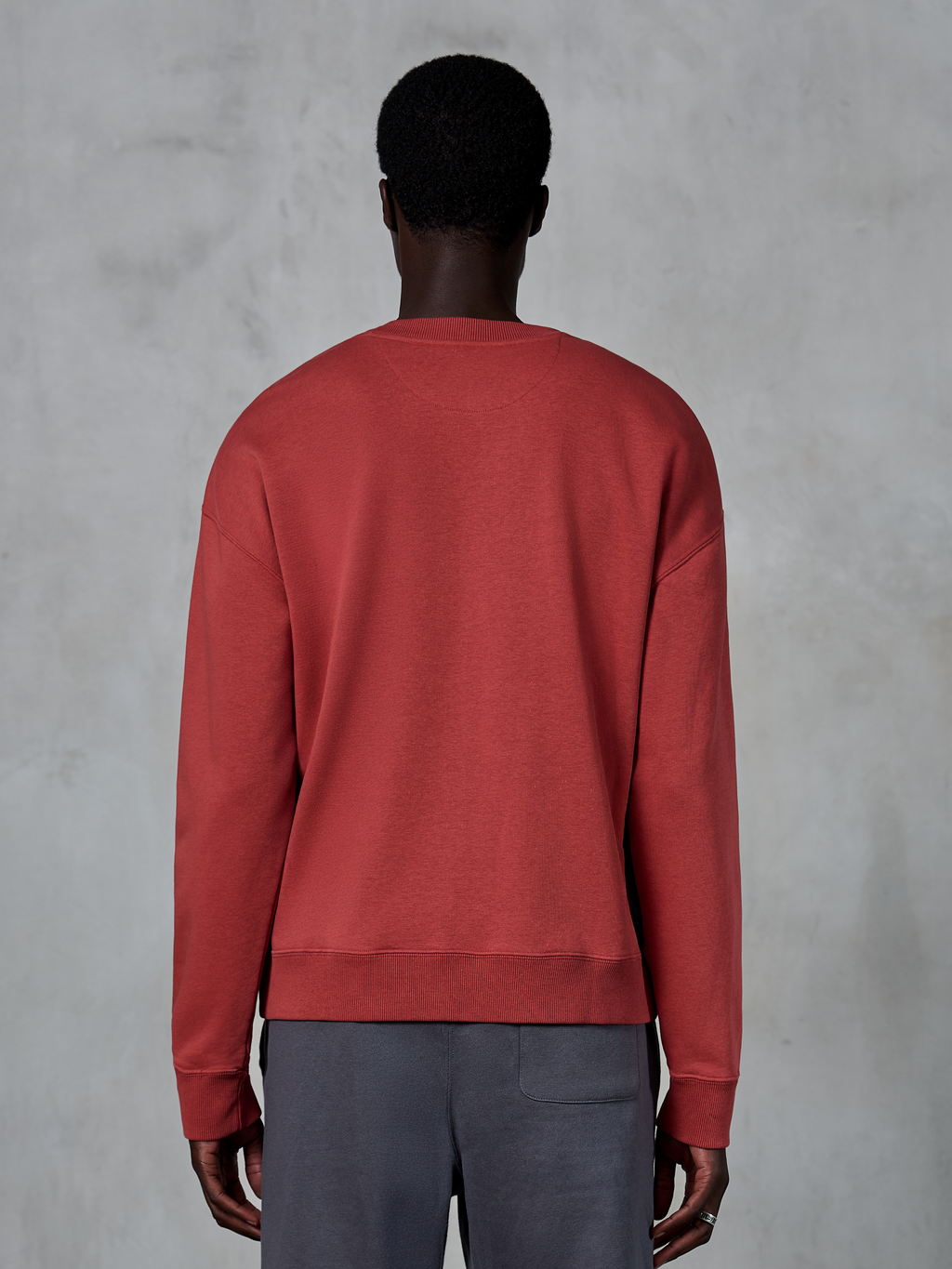 Alpinestars Essentials Ageless Crew, sweatshirt de gola redonda em vermelho tijolo, vista traseira de modelo a usar camisola de corte descontraído, gola e punhos canelados, streetwear casual inspirado no desporto motorizado