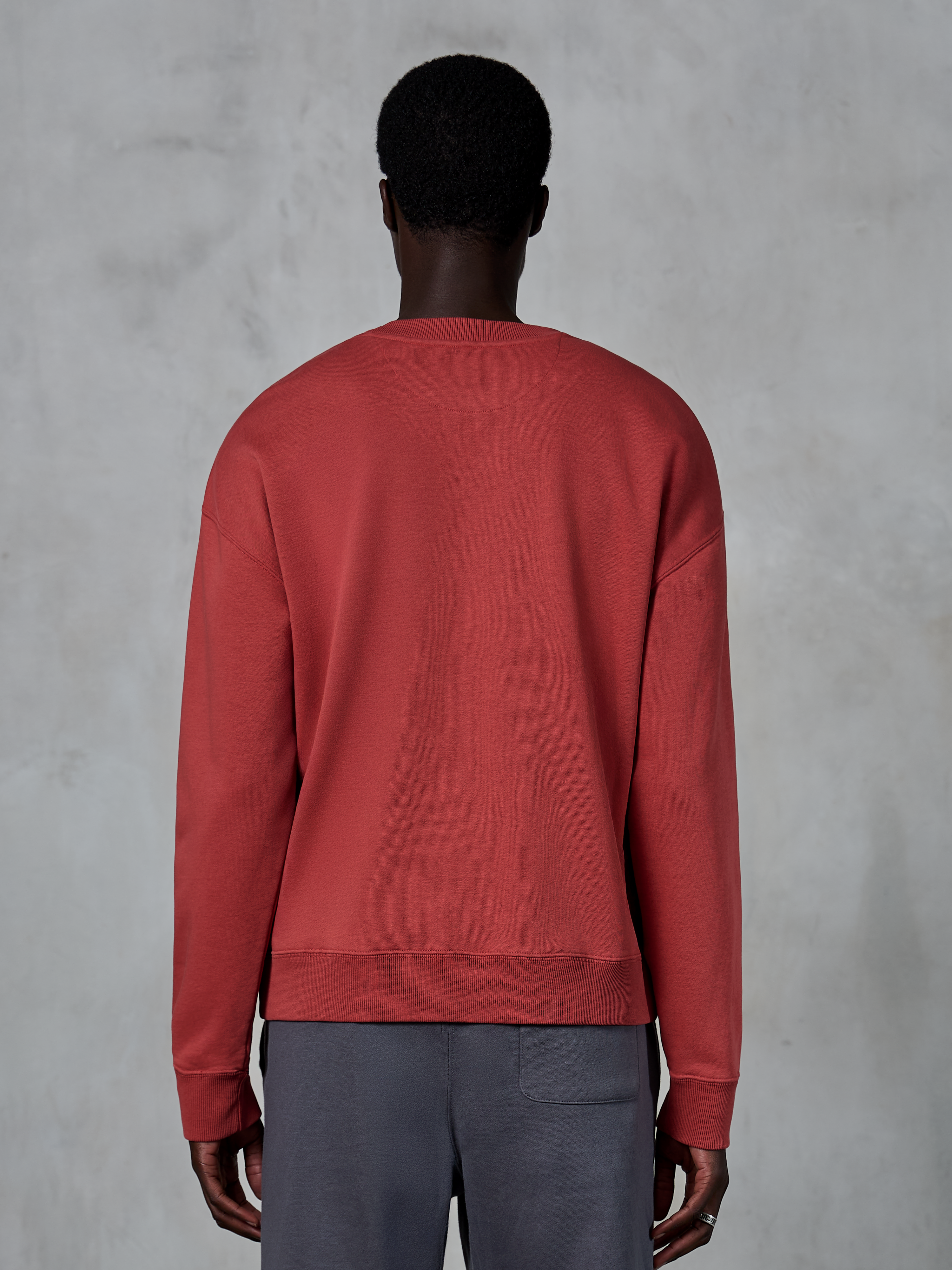 Alpinestars Essentials Ageless Crew, sweatshirt de gola redonda em vermelho tijolo, vista traseira de modelo a usar camisola de corte descontraído, gola e punhos canelados, streetwear casual inspirado no desporto motorizado