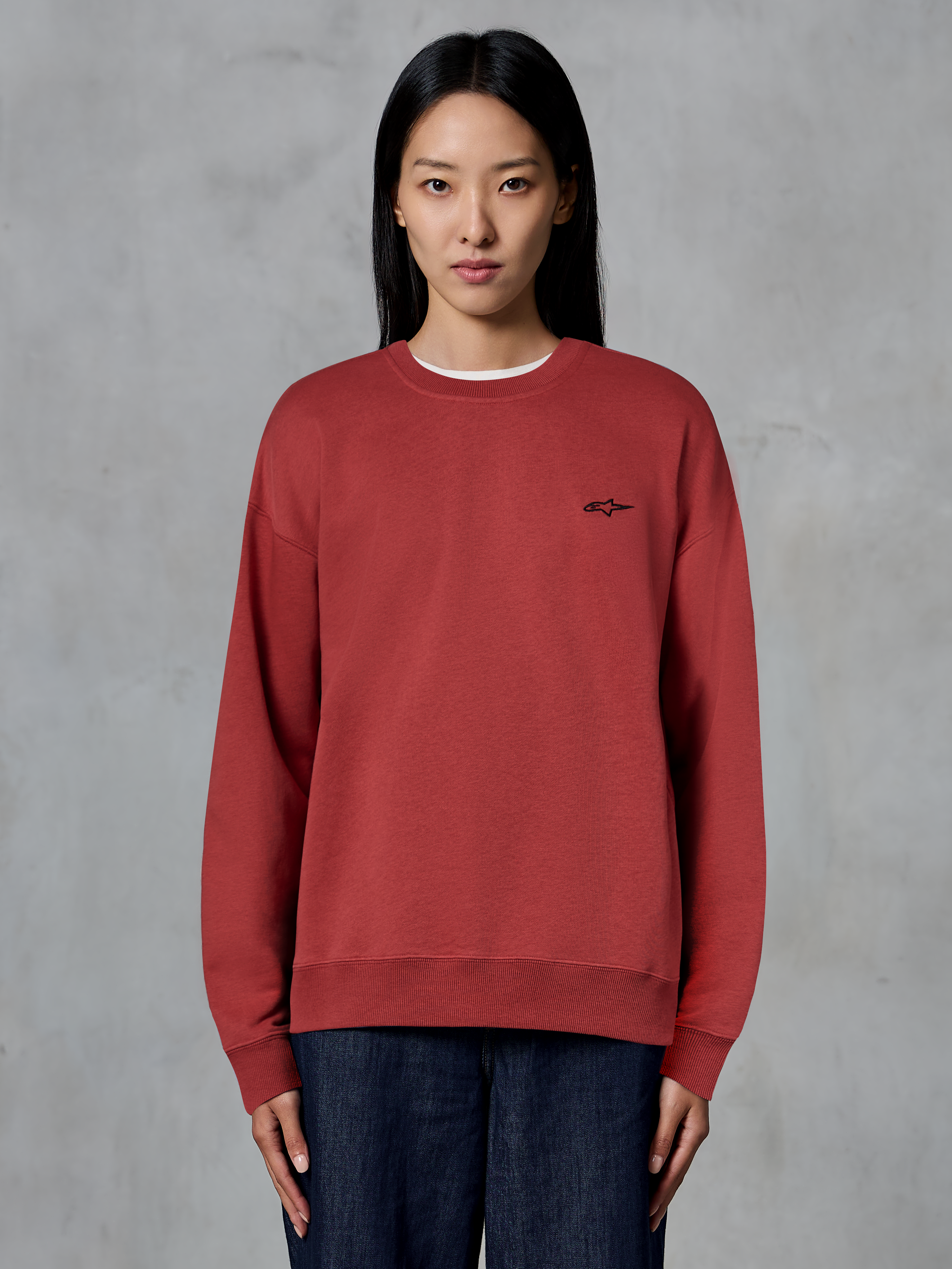 Alpinestars Essentials Ageless Crew, sweatshirt de gola redonda vermelho tijolo, pequeno logótipo preto no peito, fleece premium, vestida por modelo, streetwear casual inspirado no desporto motorizado
