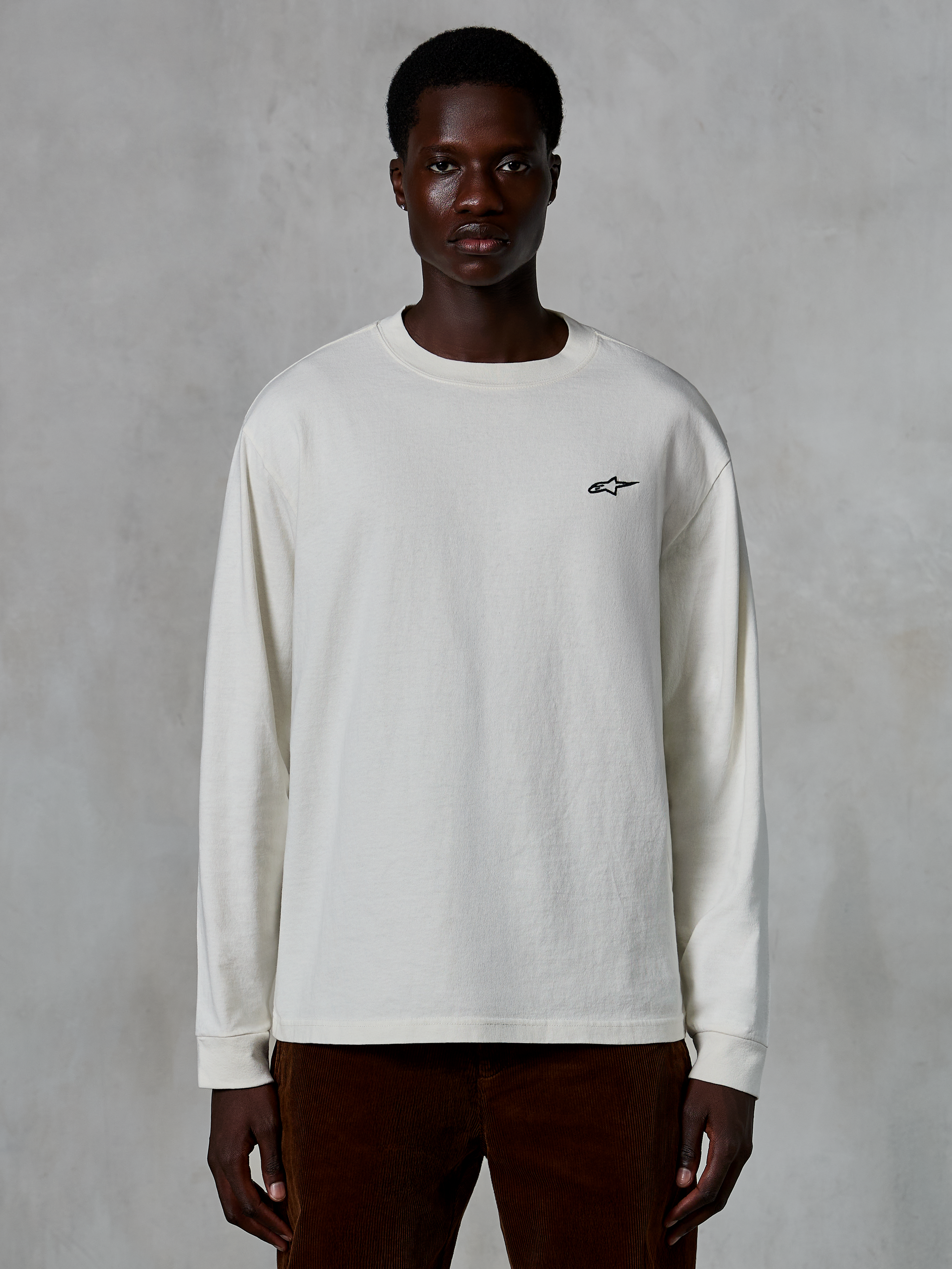 Alpinestars Essentials Ageless LS Tee, t-shirt de manga comprida, Off White, pequeno logótipo de estrela preto no peito, streetwear casual, corte relaxado, vestida por um modelo