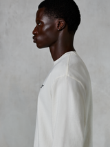 Alpinestars Essentials Ageless LS Tee, t-shirt de manga comprida, Off White, vista de perfil de um homem a usar a t-shirt de ajuste descontraído, com um pequeno logótipo preto no peito, vestuário de estilo de vida casual inspirado no desporto motorizado