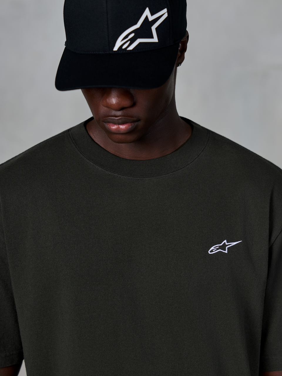 Alpinestars Essentials Ageless SS Tee, t-shirt de manga curta, em preto, com um pequeno logótipo Alpinestars branco no peito, usada com um boné de basebol preto com logótipo, estilo streetwear casual de desportos motorizados