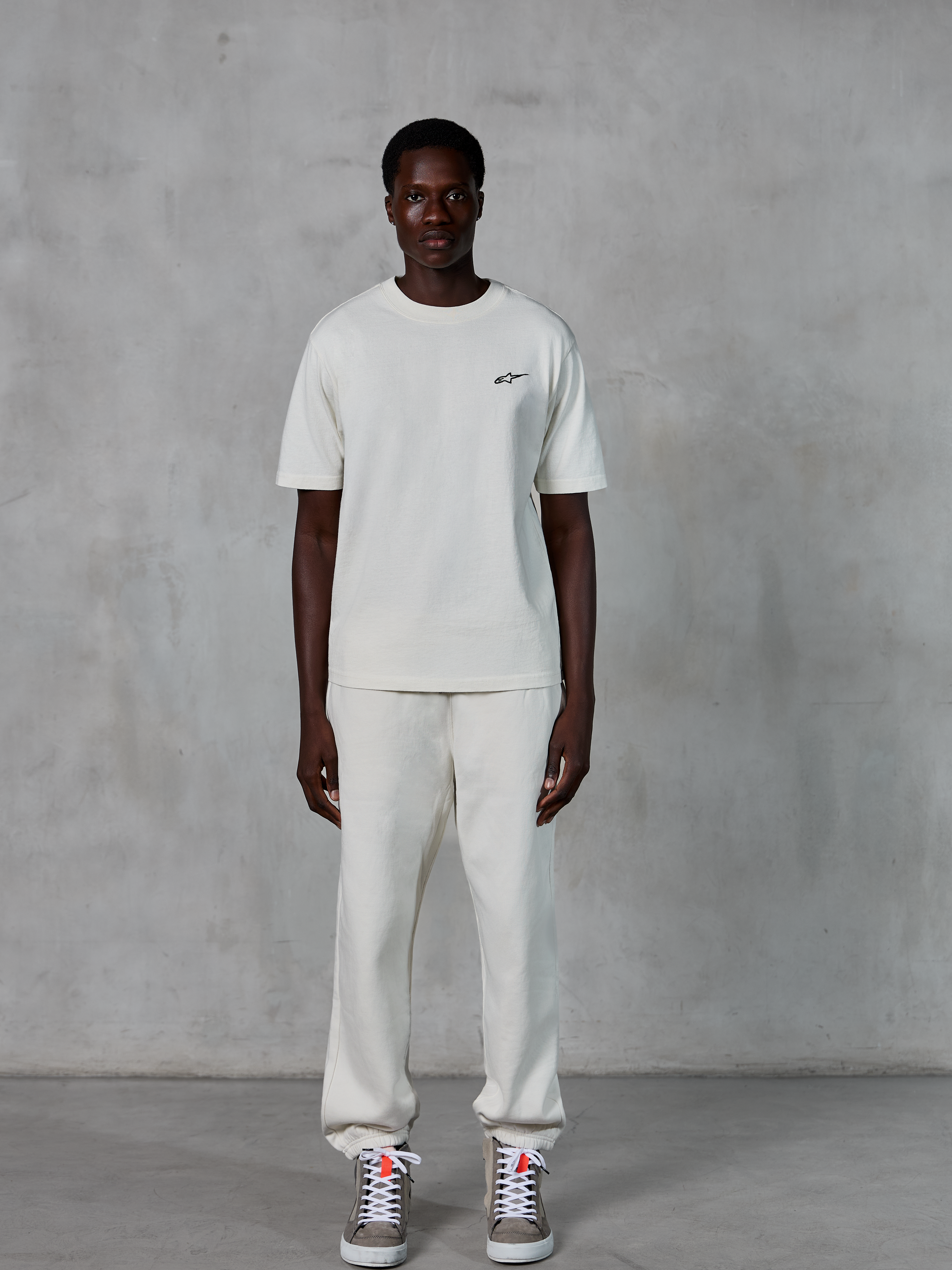 Alpinestars Essentials Ageless SS Tee, t-shirt de manga curta, Off White, com um pequeno logótipo Alpinestars preto no peito, combinada com calças joggers a condizer e sapatilhas para um visual casual e descontraído