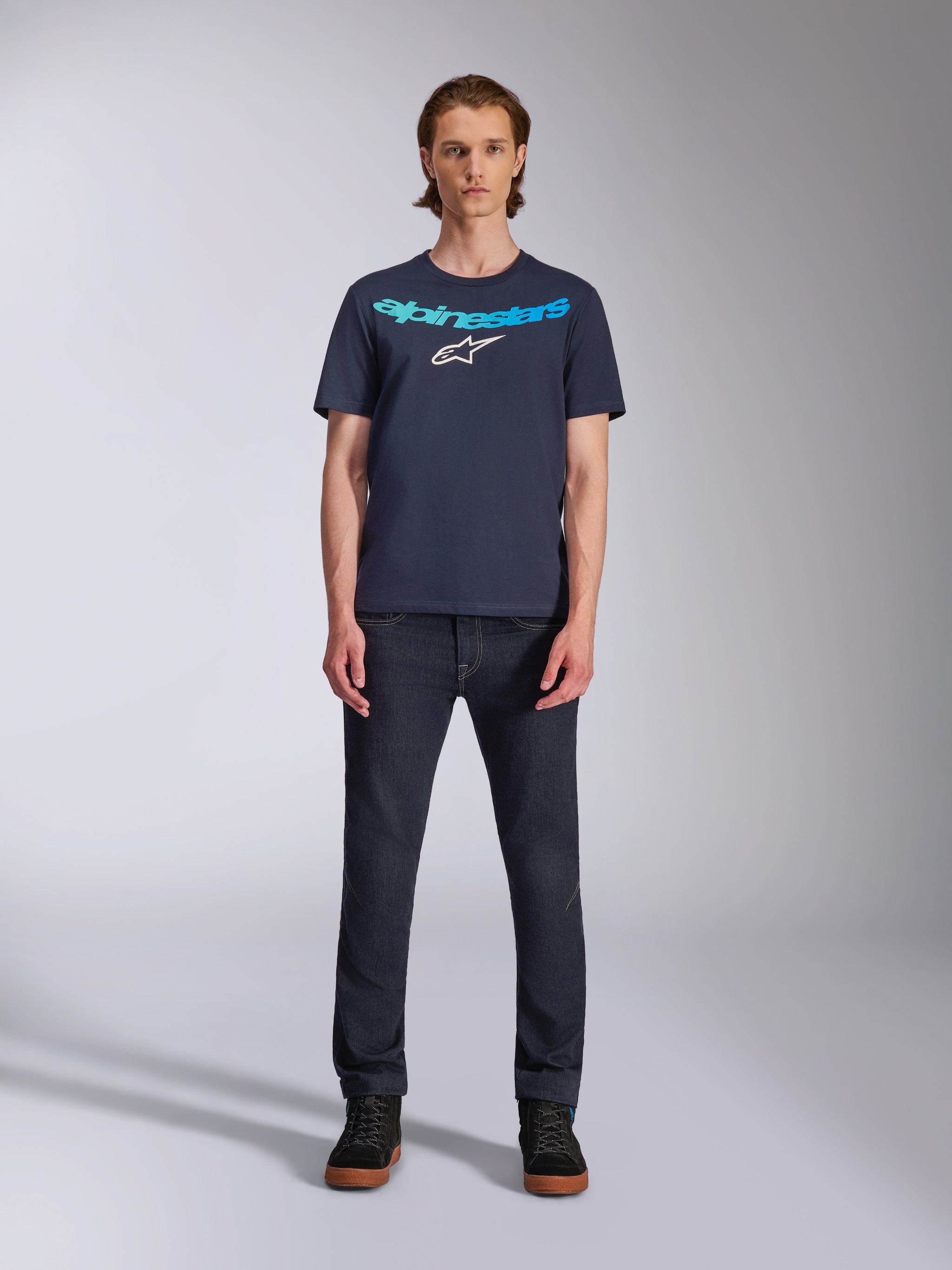 Alpinestars Collared CSF Tee, T-shirt de manga curta, azul marinho, com texto Alpinestars em azul claro e logótipo de estrela branco no peito, vestida por modelo com calças de ganga escuras, estilo casual motorsport streetwear