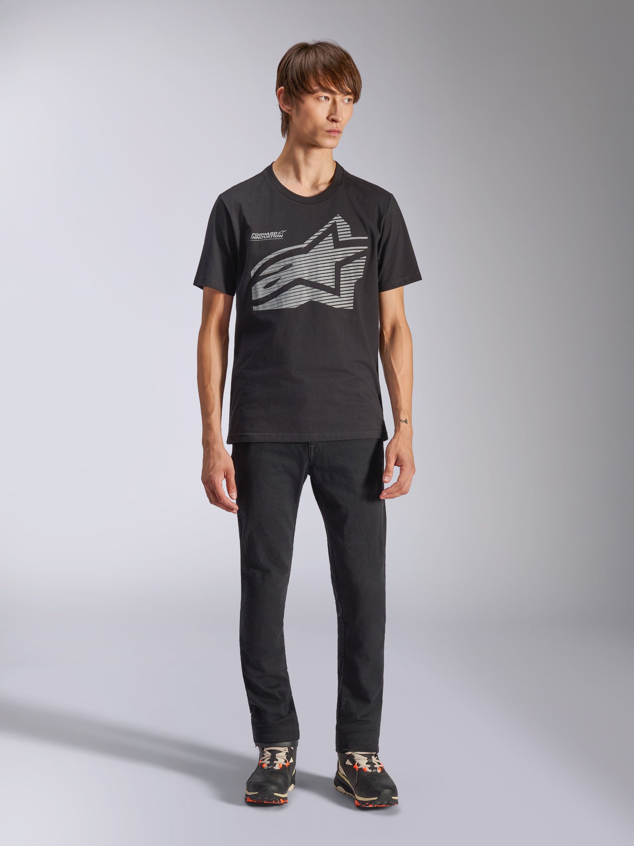 Alpinestars Fasting CSF Tee, t-shirt de manga curta, preta, logótipo Astars geométrico grande em cinzento, usada por modelo com calças pretas e sapatilhas, streetwear casual de motorsport