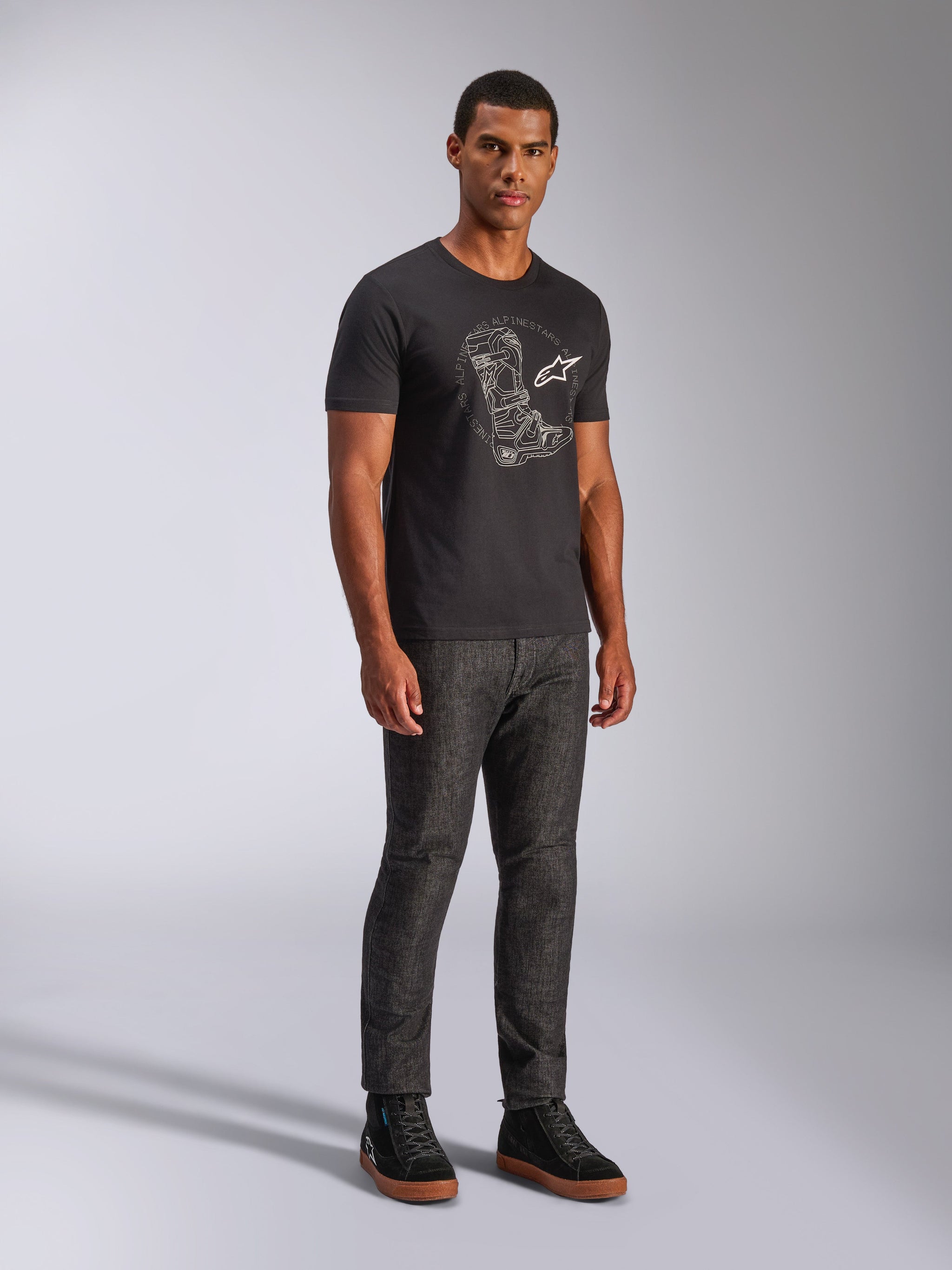 Alpinestars Tech Boot CSF Tee, T-shirt de manga curta, preta, com um gráfico branco de uma bota técnica e logótipo no peito, vestida por um modelo com calças de ganga escuras e sapatilhas pretas, streetwear casual inspirado no desporto motorizado