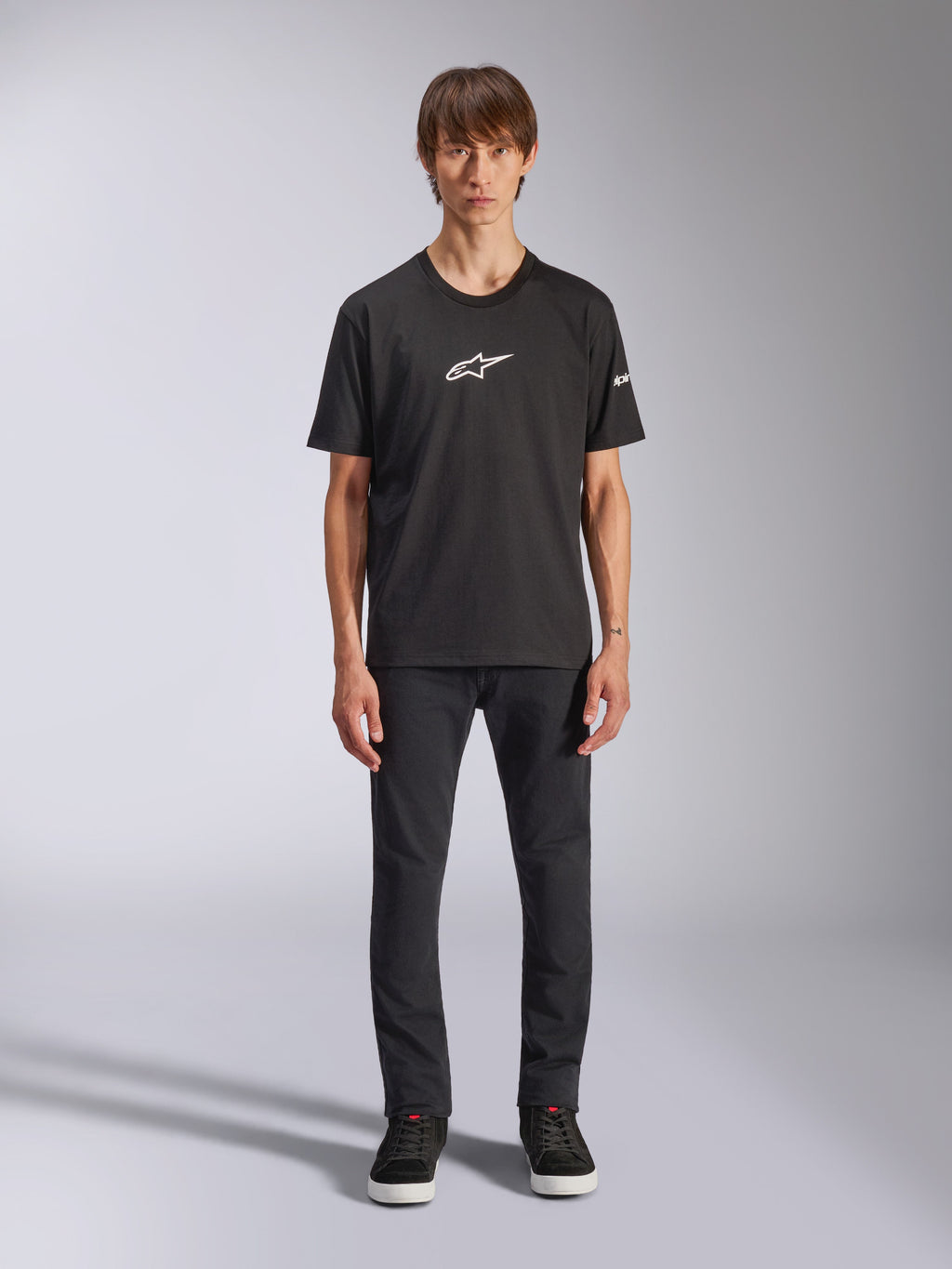 T-shirt Alpinestars Frontal CSF, t-shirt de manga curta, preta, logótipo Alpinestars branco no peito, vestida por um modelo com calças pretas e sapatos pretos, vestuário desportivo de performance casual