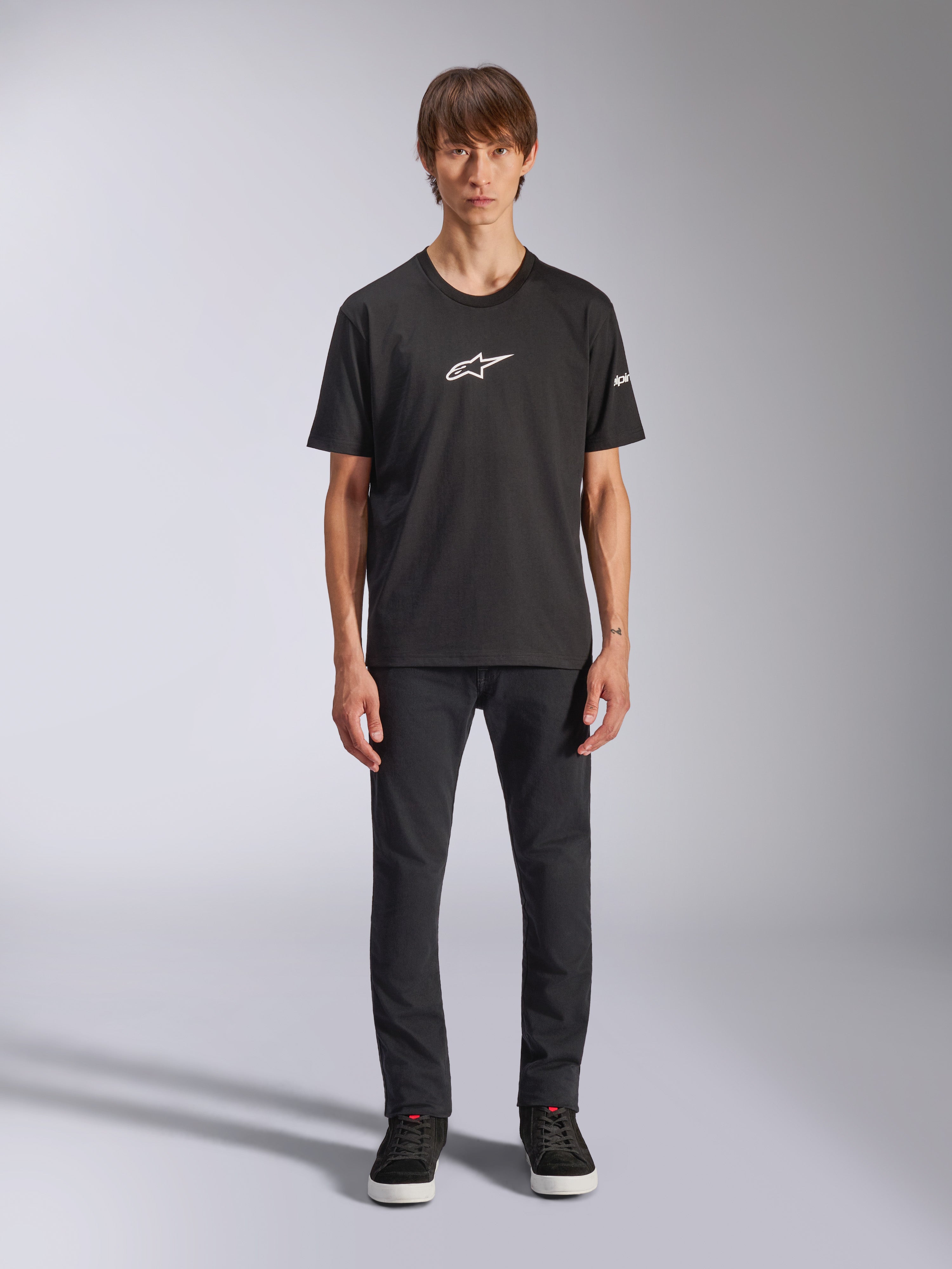 T-shirt Alpinestars Frontal CSF, t-shirt de manga curta, preta, logótipo Alpinestars branco no peito, vestida por um modelo com calças pretas e sapatos pretos, vestuário desportivo de performance casual