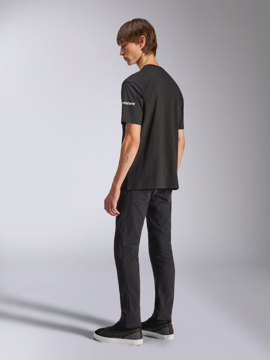 Alpinestars Frontal CSF Tee, t-shirt de manga curta, preta, marca astars branca na manga, usada por modelo com calças e sapatos pretos, design casual inspirado no desporto motorizado