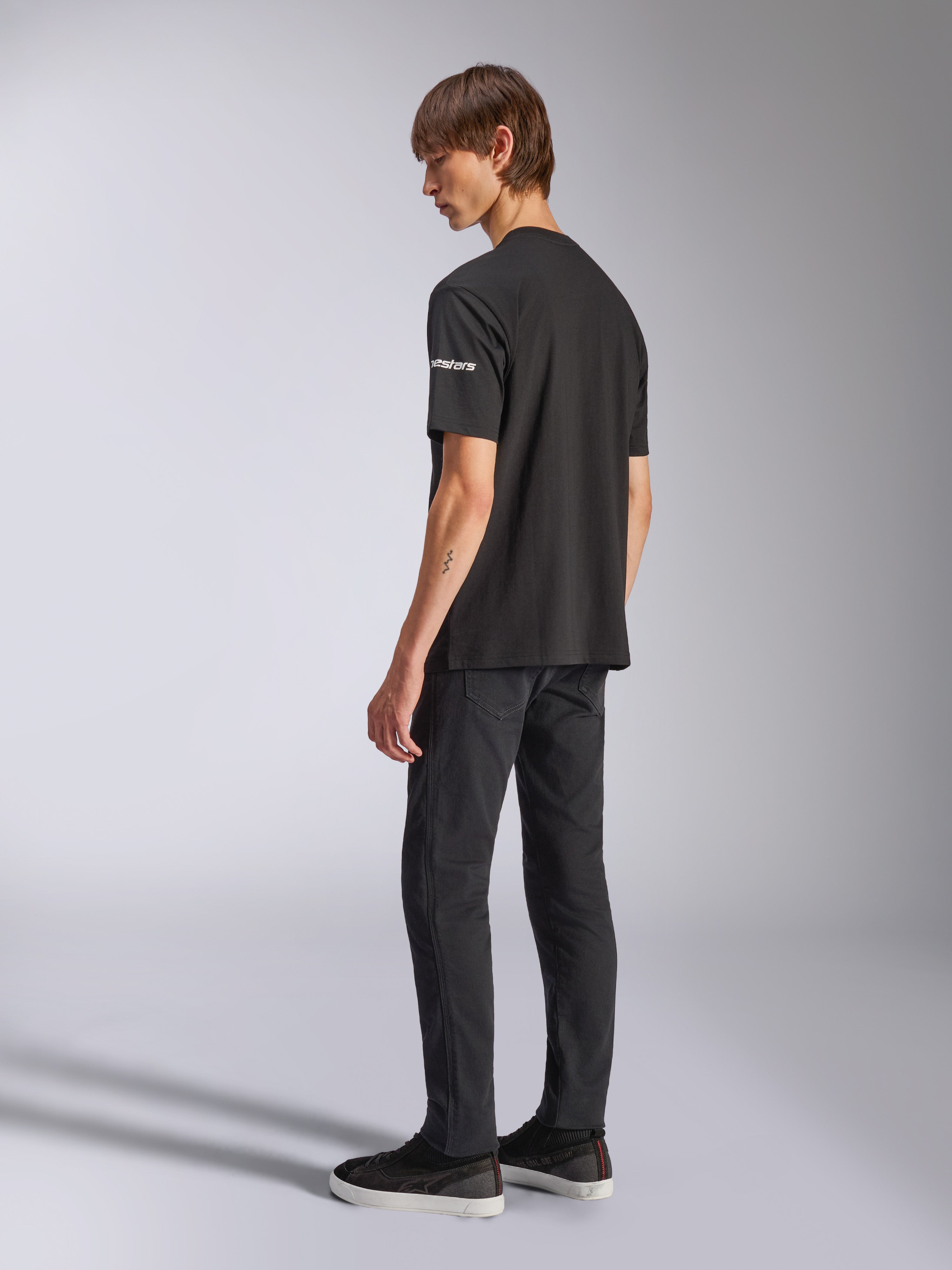 Alpinestars Frontal CSF Tee, t-shirt de manga curta, preta, marca astars branca na manga, usada por modelo com calças e sapatos pretos, design casual inspirado no desporto motorizado