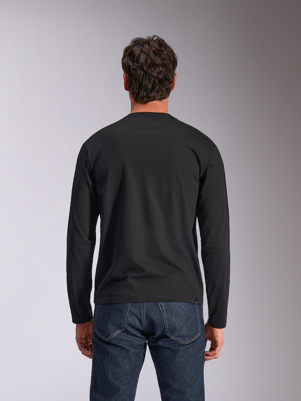 Alpinestars Trackside CSF Tee, t-shirt de manga comprida, preta, vista traseira, usada com calças de ganga azul-escuro, streetwear casual inspirado no desporto motorizado