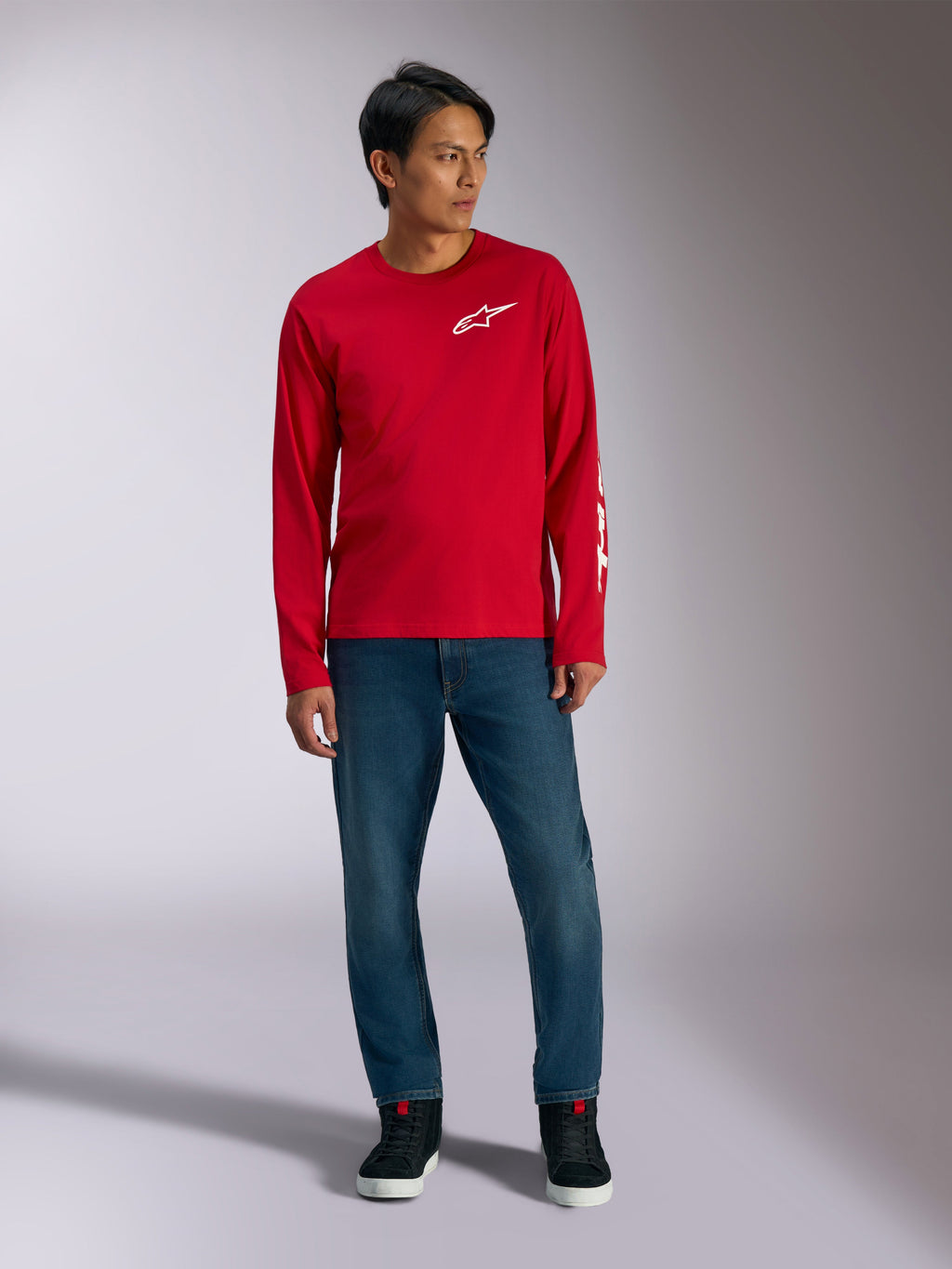 Alpinestars Trackside CSF Tee, T-shirt de manga comprida, vermelha com logótipo Alpinestars branco, fotografia de lifestyle usada com calças de ganga azuis e sapatilhas pretas, vestuário desportivo casual inspirado no desporto motorizado