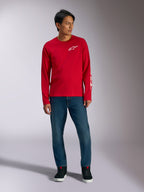 Alpinestars Trackside CSF Tee, T-shirt de manga comprida, vermelha com logótipo Alpinestars branco, fotografia de lifestyle usada com calças de ganga azuis e sapatilhas pretas, vestuário desportivo casual inspirado no desporto motorizado