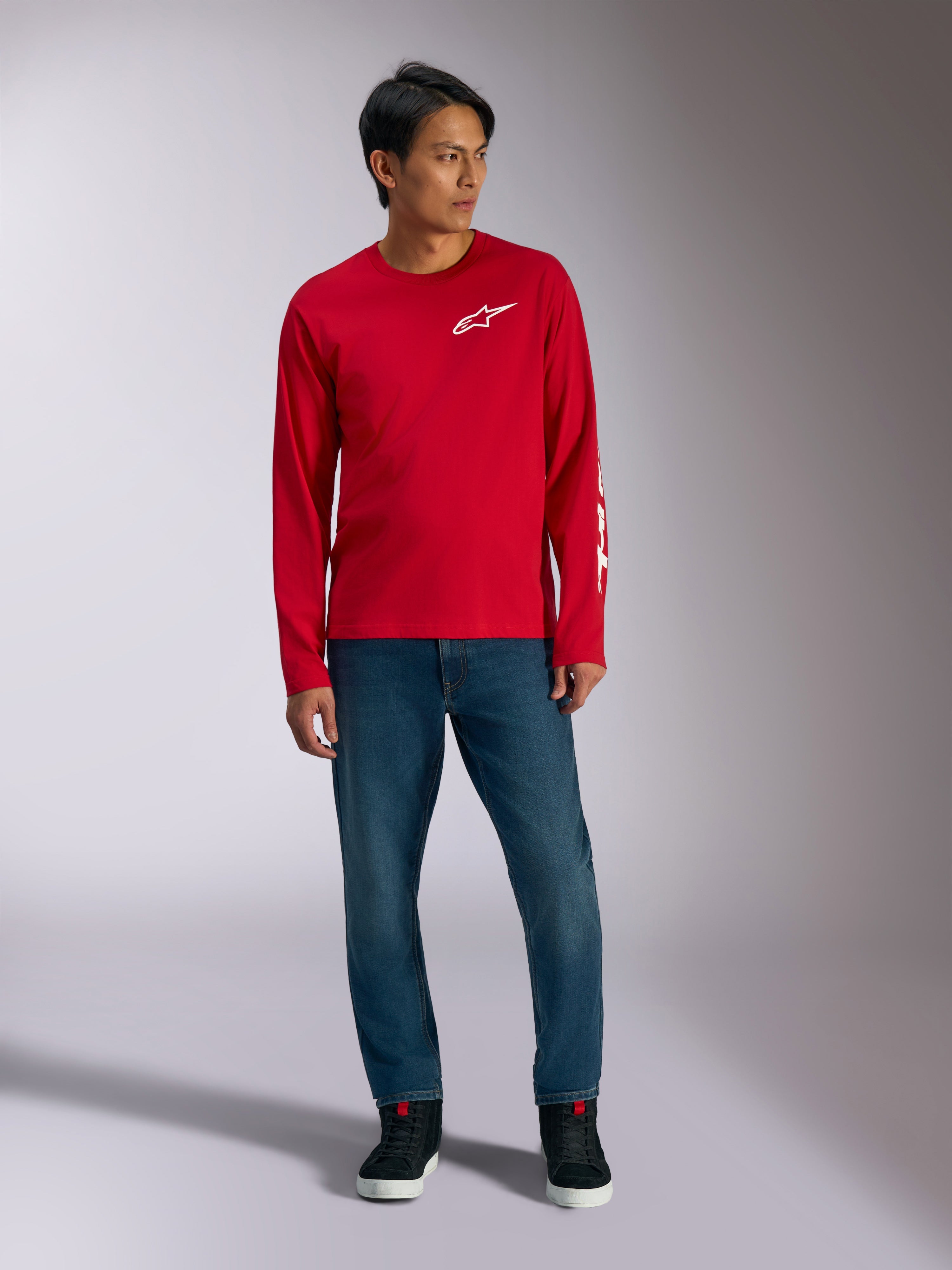 Alpinestars Trackside CSF Tee, T-shirt de manga comprida, vermelha com logótipo Alpinestars branco, fotografia de lifestyle usada com calças de ganga azuis e sapatilhas pretas, vestuário desportivo casual inspirado no desporto motorizado