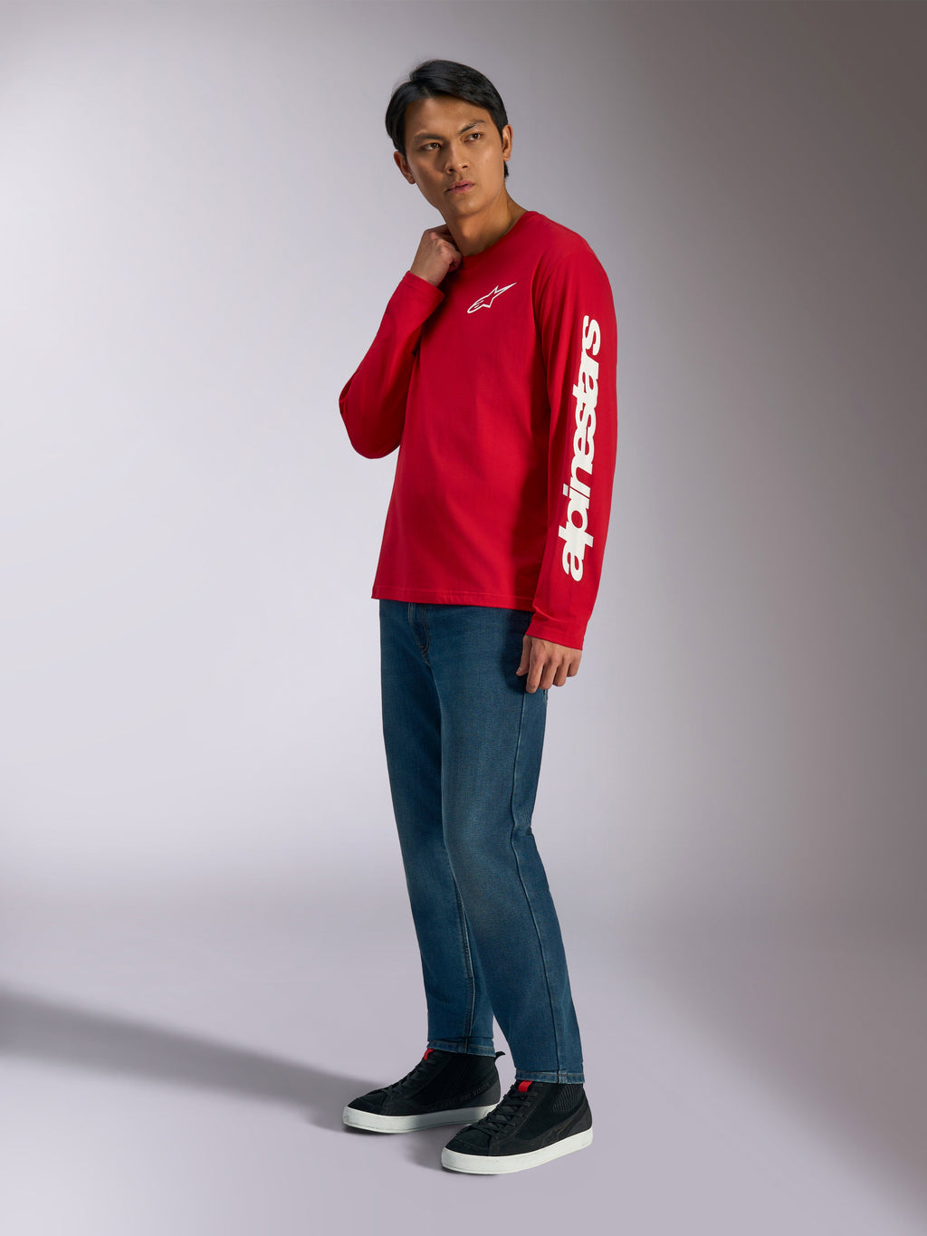 T-shirt de manga comprida Alpinestars Trackside CSF, vermelha com logótipos Alpinestars brancos no peito e na manga, usada por modelo com calças de ganga azuis e sapatilhas pretas, streetwear casual inspirado no desporto motorizado