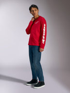 T-shirt de manga comprida Alpinestars Trackside CSF, vermelha com logótipos Alpinestars brancos no peito e na manga, usada por modelo com calças de ganga azuis e sapatilhas pretas, streetwear casual inspirado no desporto motorizado