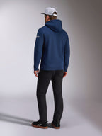 Alpinestars Frontal Hoodie, vista traseira de um hoodie de lã polar azul-marinho, logótipo branco na manga, combinado com calças pretas e um boné trucker de rede branco, streetwear casual inspirado no desporto motorizado