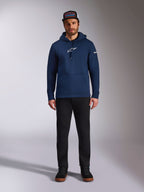 Modelo masculino a usar o Hoodie Frontal da Alpinestars em azul-marinho, sweatshirt de lã polar com logótipo Astars branco no peito e logótipo da marca na manga, com bolso tipo canguru e capuz com cordão, combinado com calças pretas e boné da marca, streetwear casual de desporto motorizado