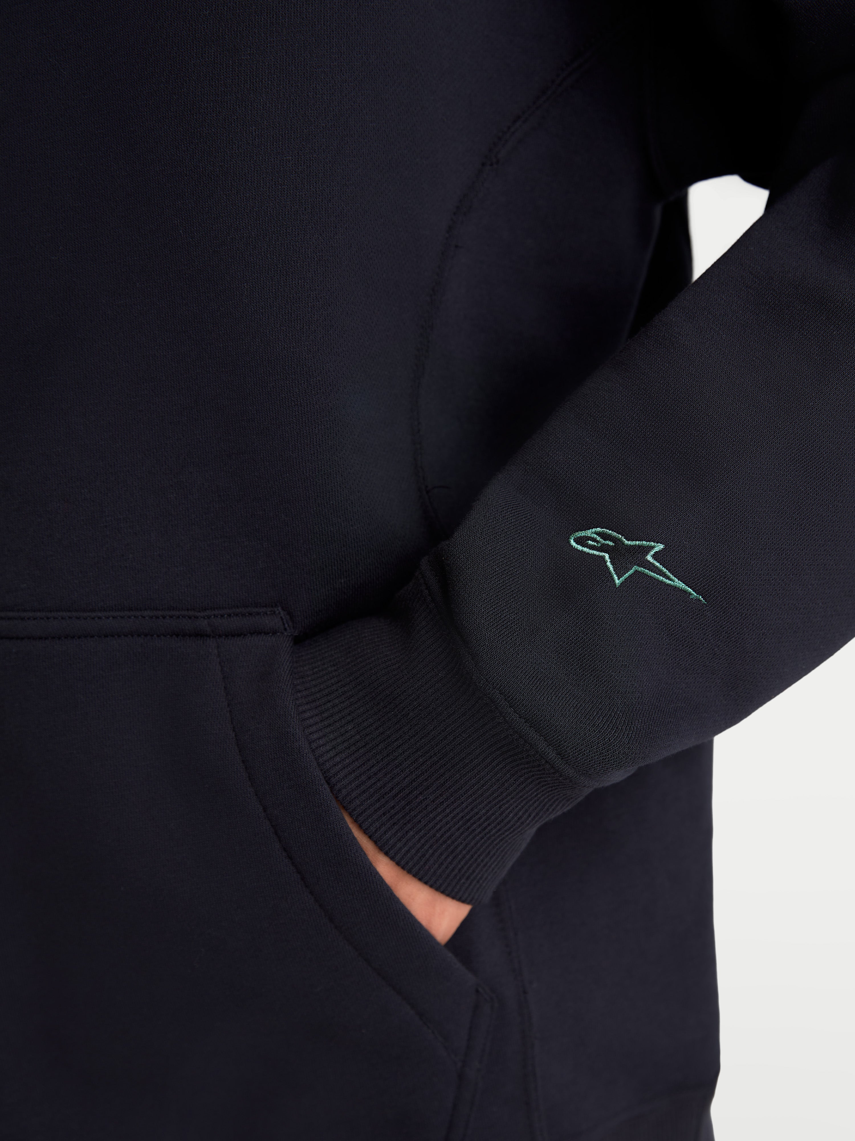 Alpinestars Guise Oversized Crew, Black Sportswear Fleece Pullover, detailed view showing the sleeve with a teal embroidered Astars logo, ribbed cuff, and kangaroo pocket entry, premium cotton and recycled polyester blend sweatshirt.