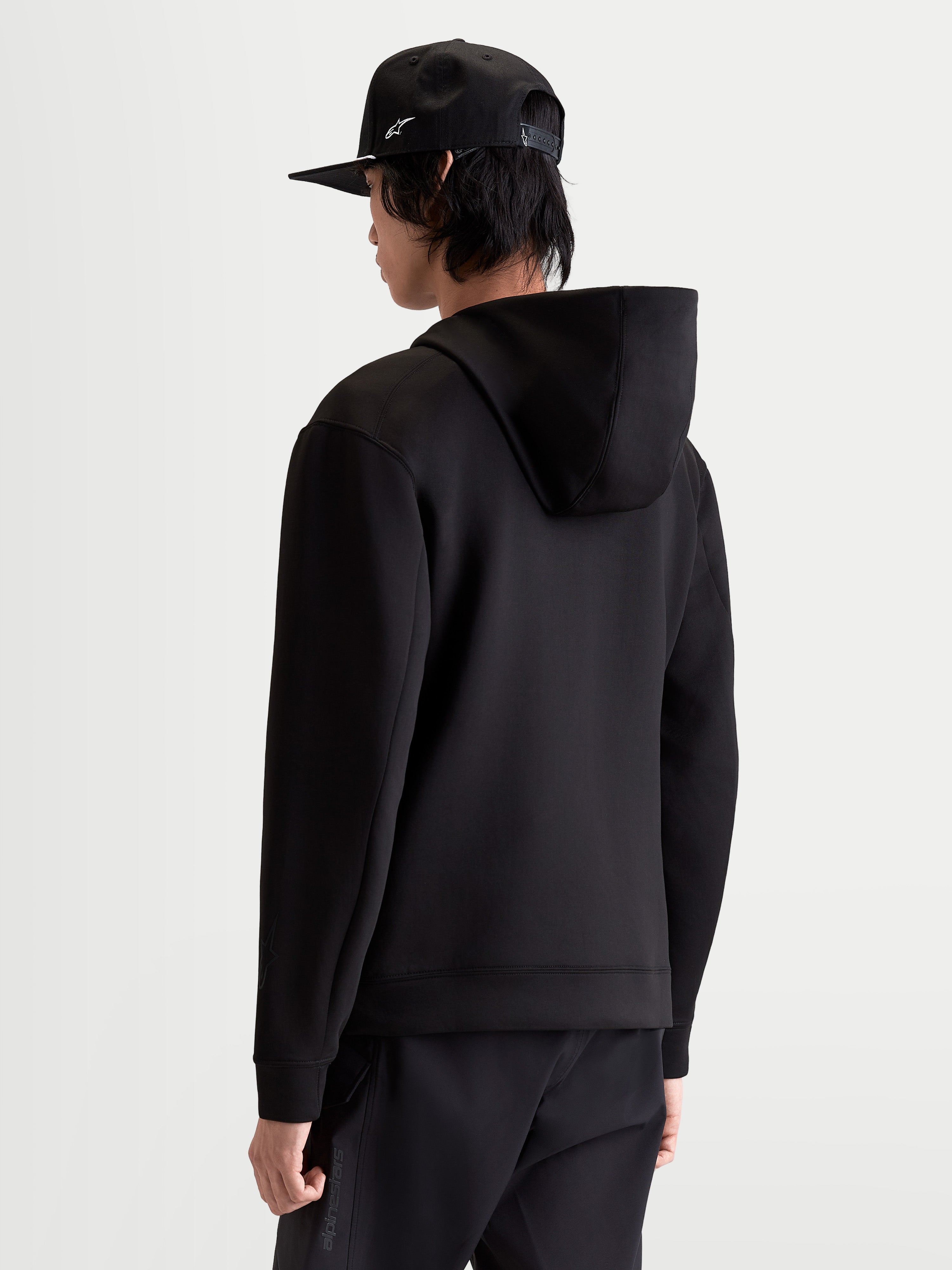 Alpinestars Camisola Com Capuz Datrix, camisola com capuz preta para homem, vista traseira no modelo mostrando a construção em fleece de dupla face e o capuz forrado em malha, para um estilo casual inspirado no motorsport.