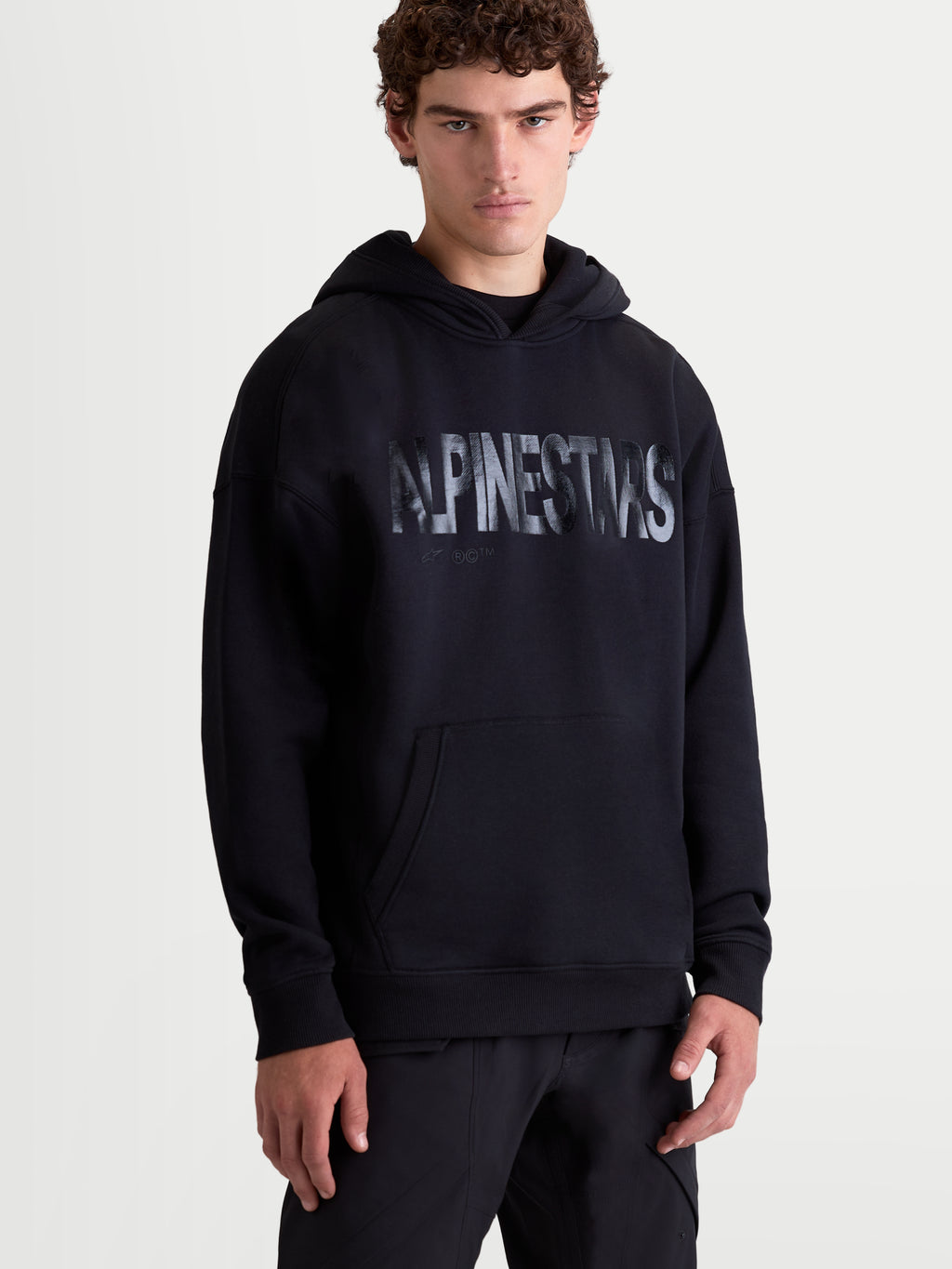 Alpinestars Camisola com Capuz Shaw Oversized, hoodie de estilo sportswear para homem, preta, logótipo texturizado no peito, bolso canguru e capuz forrado, fabricada em fleece de algodão e poliéster reciclado, vista frontal no modelo.