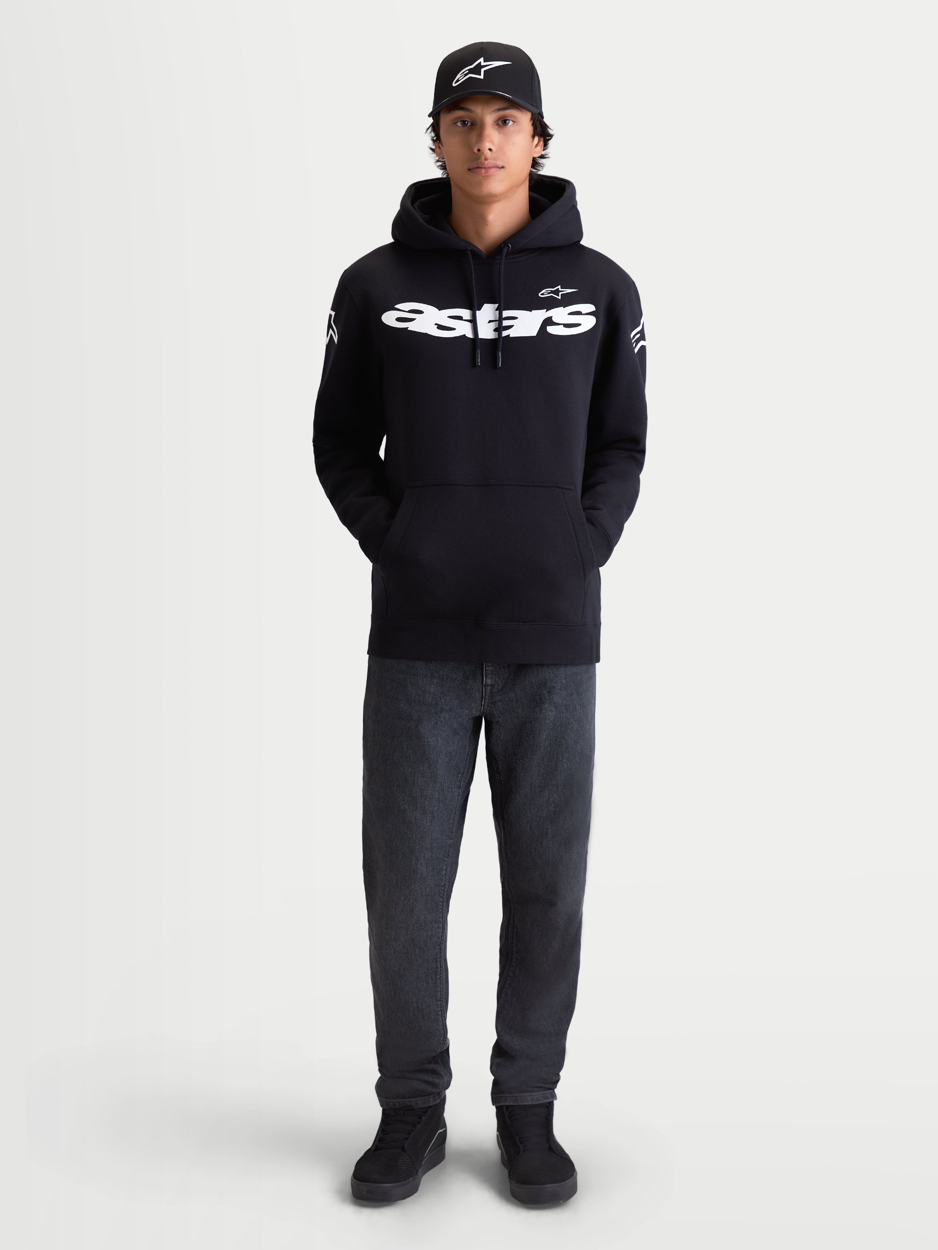 Alpinestars Camisola Com Capuz Velocifier, camisola com capuz para homem, preta, com logótipo Astars branco na frente e nos ombros, sportswear casual para uso fora da moto, modelo a usar boné e calças de ganga.