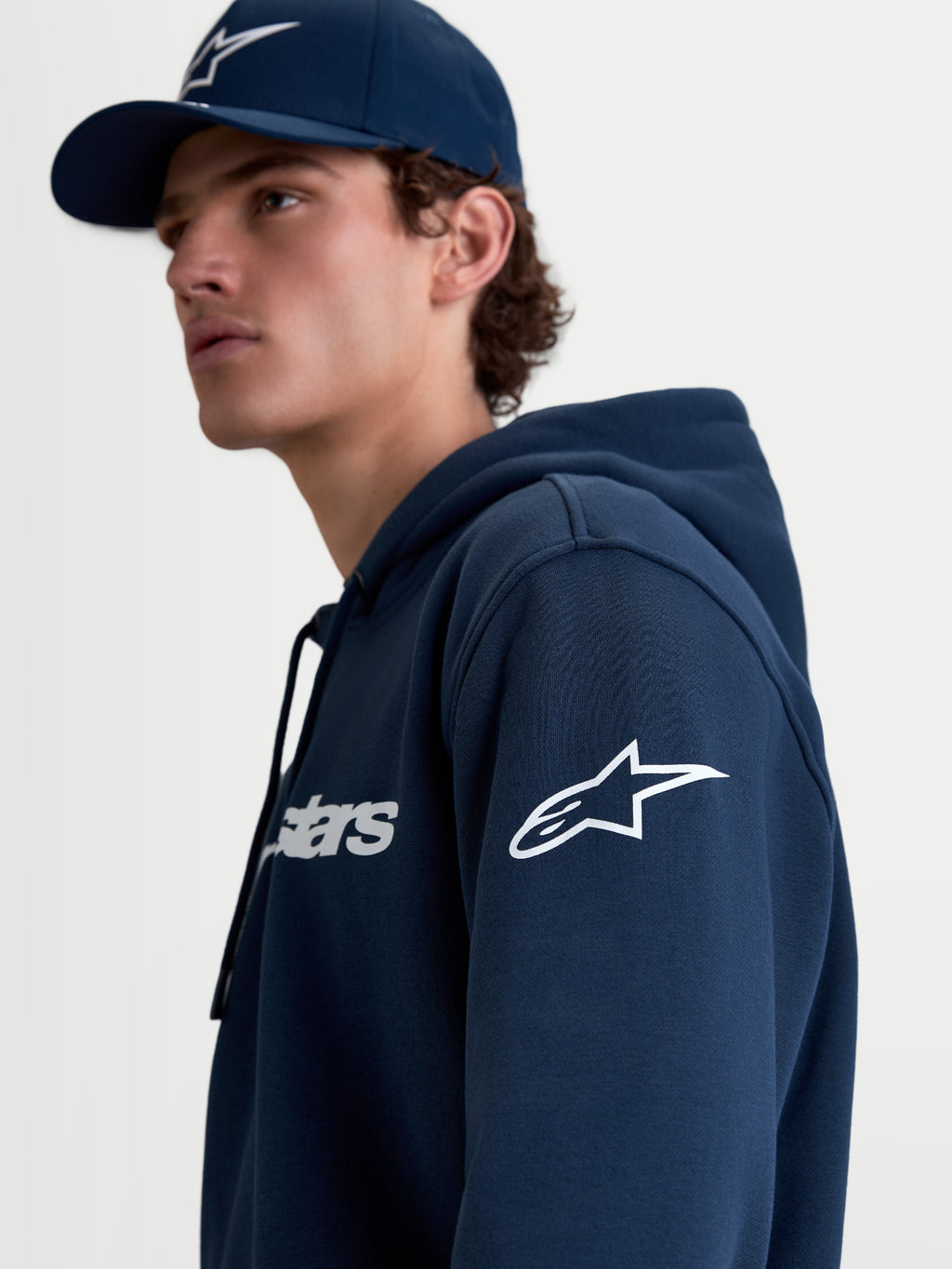 Alpinestars Camisola Com Capuz Race Wordmark, camisola de sportswear para homem em fleece, azul marinho e branca, com o logótipo Ageless na manga e logótipo Race no peito, vista de estilo de vida em modelo.