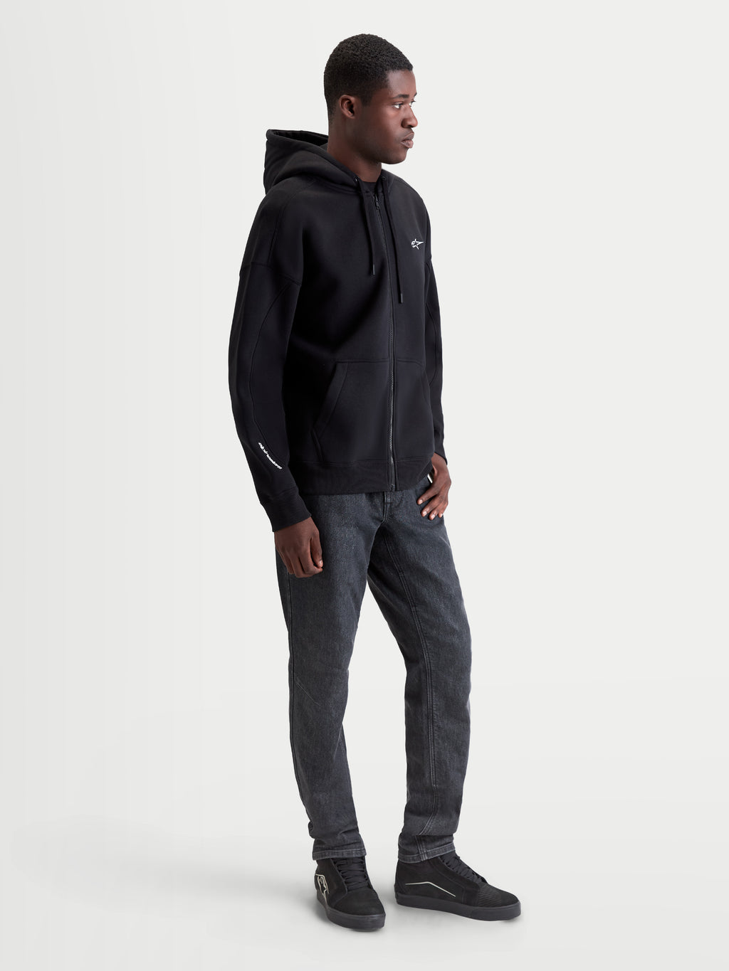 Alpinestars Entity Oversized Hoodie, Sportswear Zip-Front Fleece, Black, 80% Cotton and 20% Recycled Polyester. Features include a Vislon front zipper, kangaroo pocket, and embroidered logo on the chest and sleeve. Shown on model for a relaxed, oversized fit, ideal for casual motorsport style.