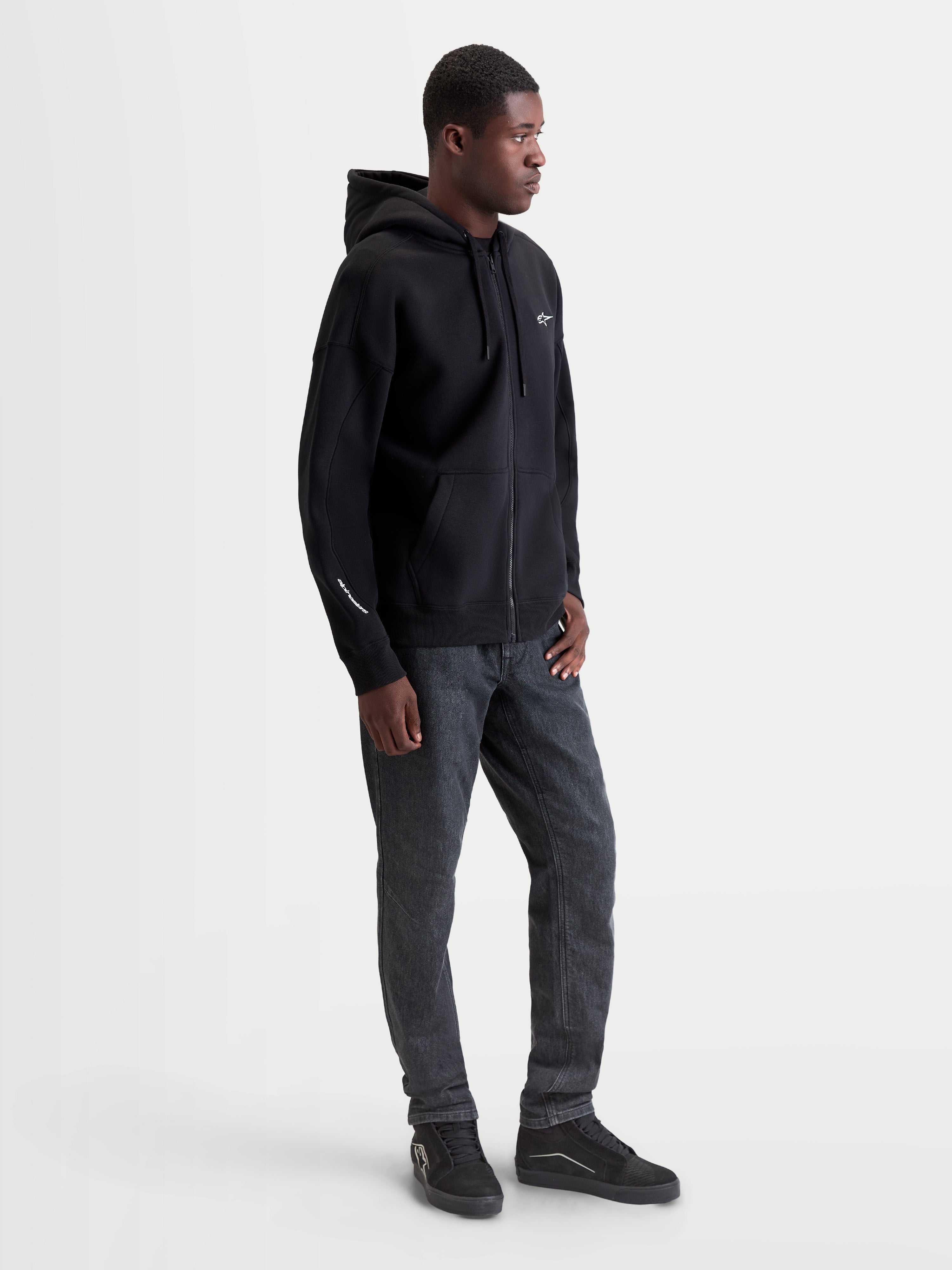 Alpinestars Entity Oversized Hoodie, Sportswear Zip-Front Fleece, Black, 80% Cotton and 20% Recycled Polyester. Features include a Vislon front zipper, kangaroo pocket, and embroidered logo on the chest and sleeve. Shown on model for a relaxed, oversized fit, ideal for casual motorsport style.