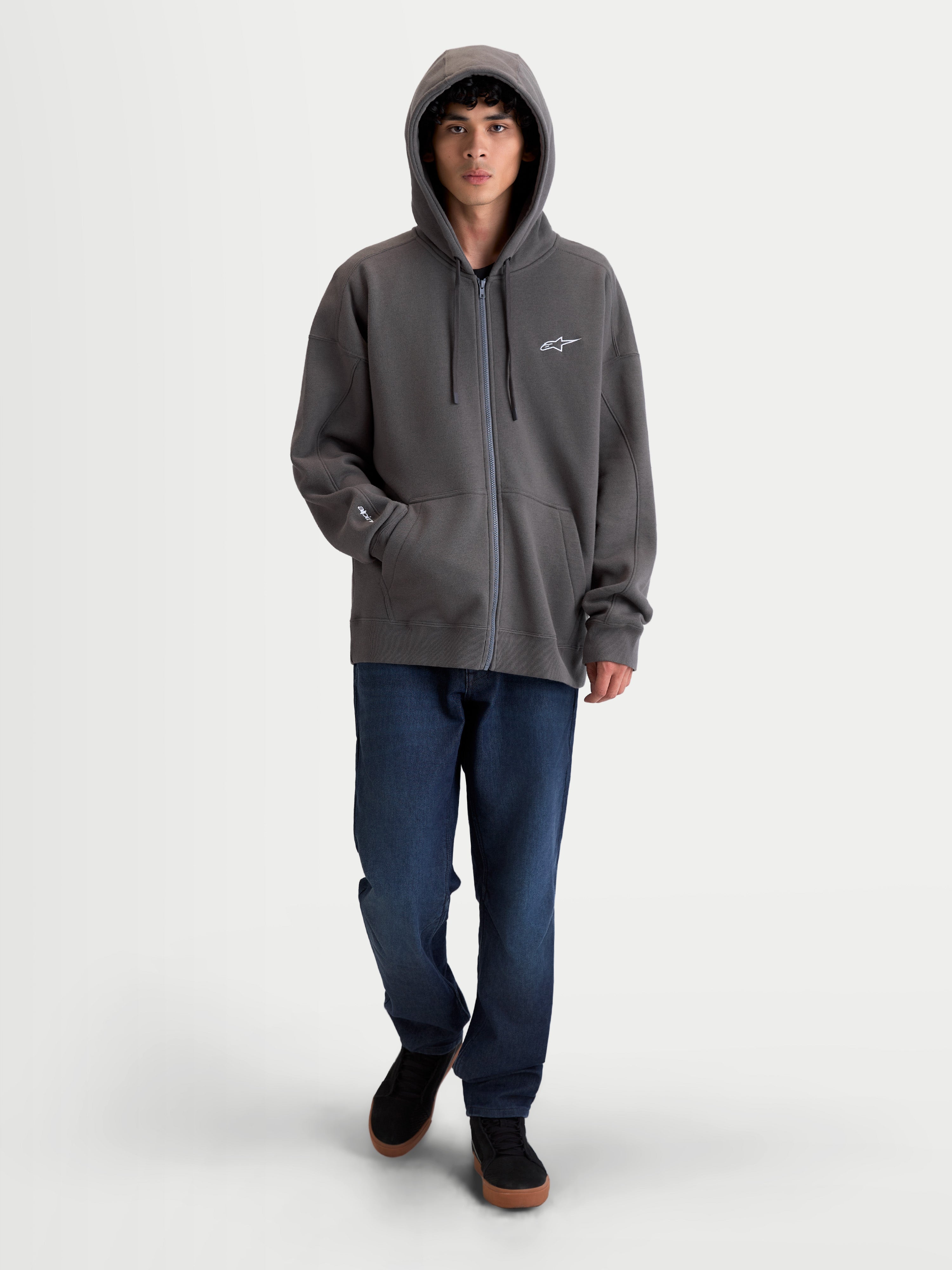 Alpinestars Camisola Com Capuz Entity Oversized, hoodie de motorsport cinzento-escuro com fecho de correr frontal Vislon, capuz com cordões e bolso canguru. Vista no modelo a exibir a silhueta oversized e descontraída com o logótipo Astars bordado no peito e na manga.