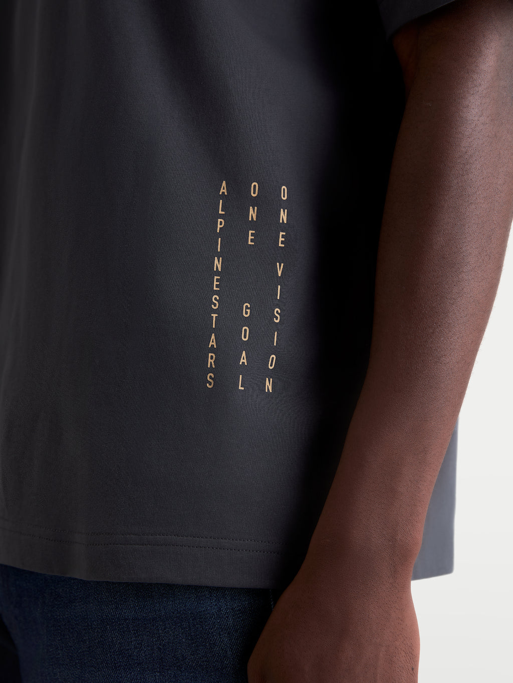 Alpinestars Chalk Oversized CSF Tee, t-shirt unissexo cinzento-escuro, pormenor em grande plano do branding lateral vertical com o manifesto ONE GOAL ONE VISION, sportswear casual de inspiração motorsport.