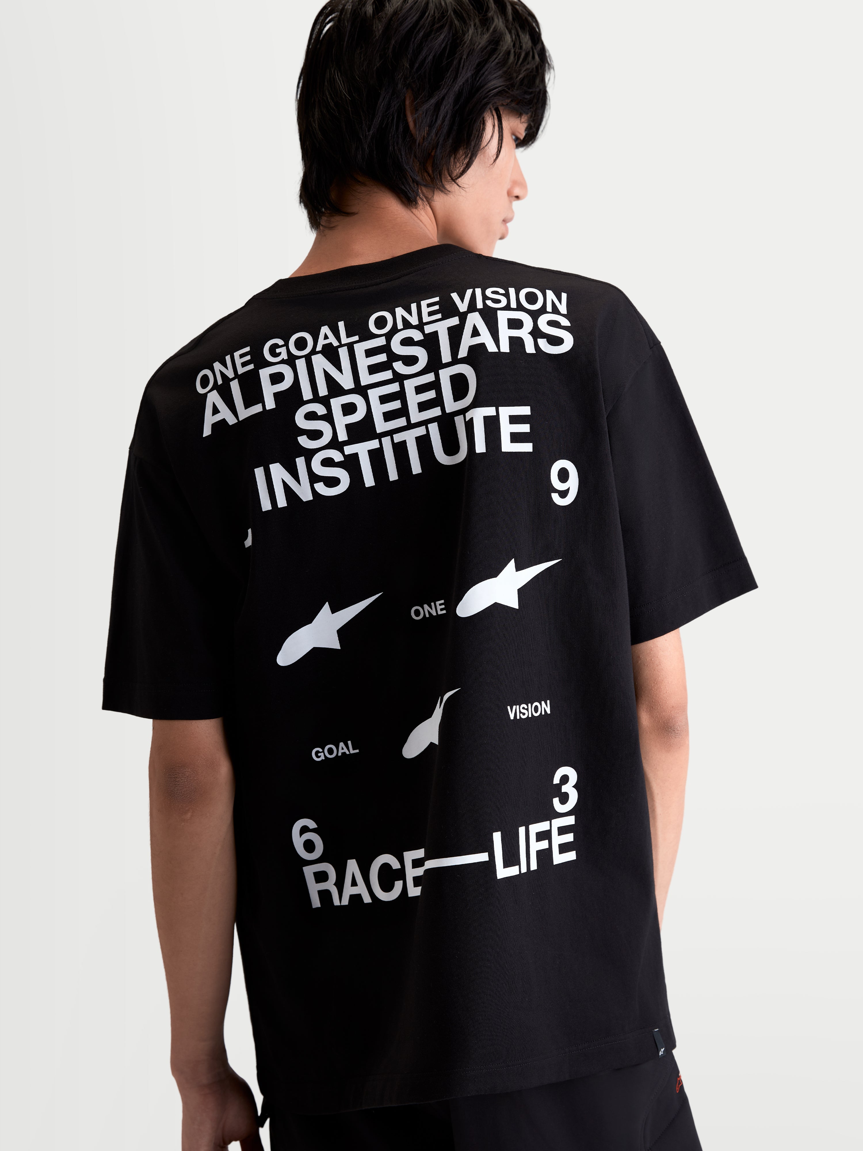 Alpinestars T-Shirt Institute Oversized CSF, t-shirt de manga curta, preta e branca, vista traseira em modelo com gráficos Alpinestars Speed Institute e Race-Life nas costas, corte oversized descontraído, sportswear inspirado no motorsport.